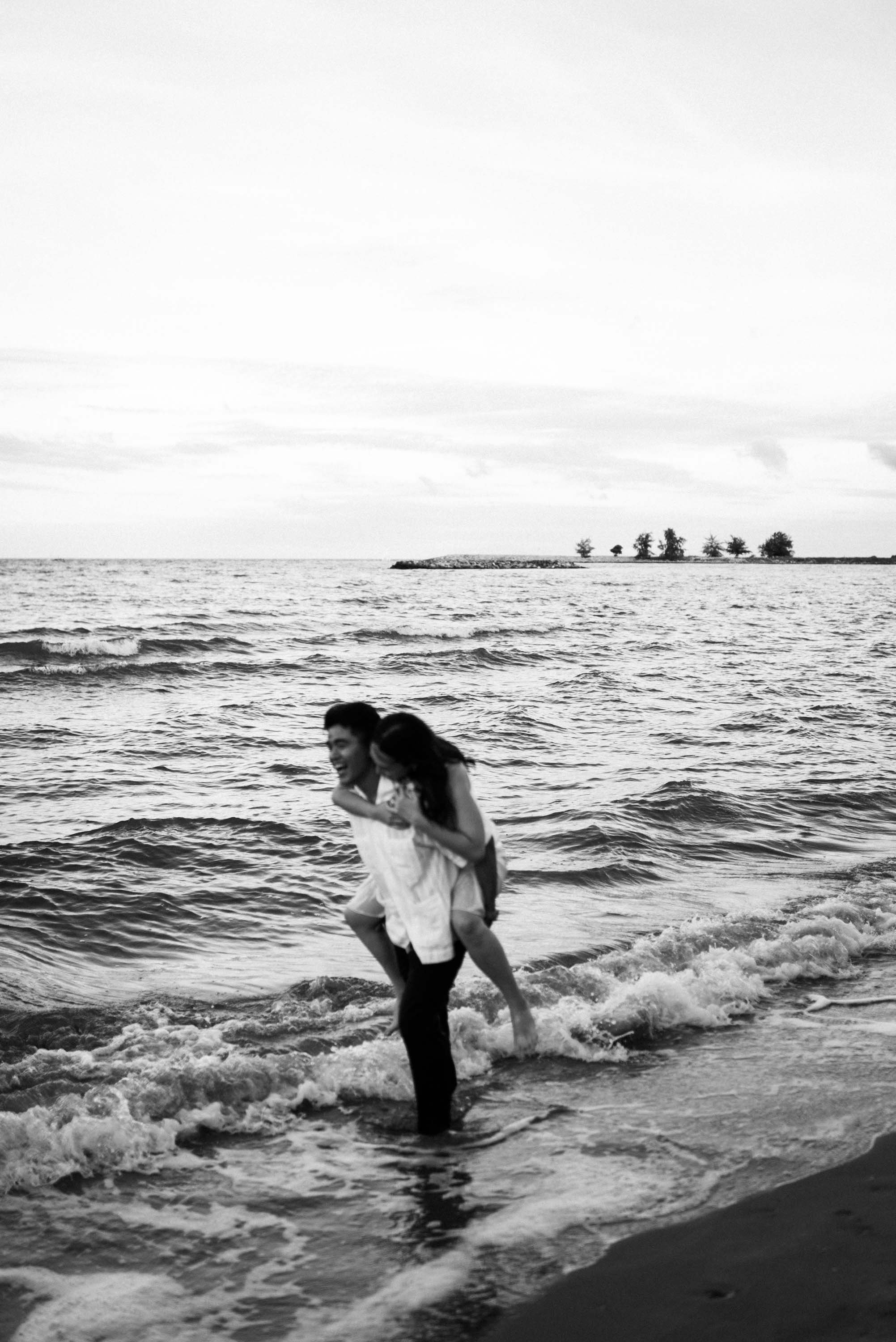 Woman riding on her partner's back as they walk along the beach.