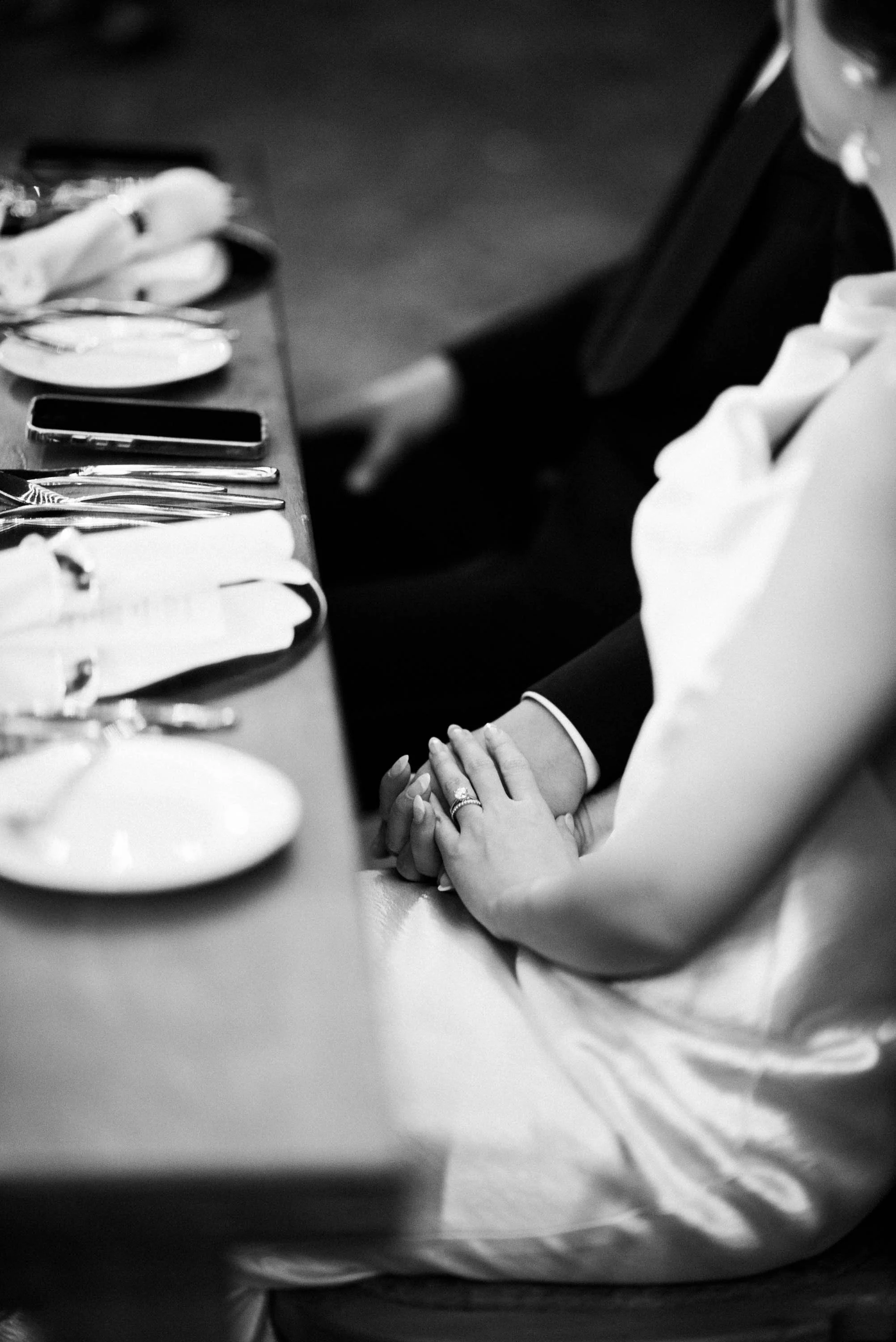 Bride and groom holding hands while listening to a guest's speech.