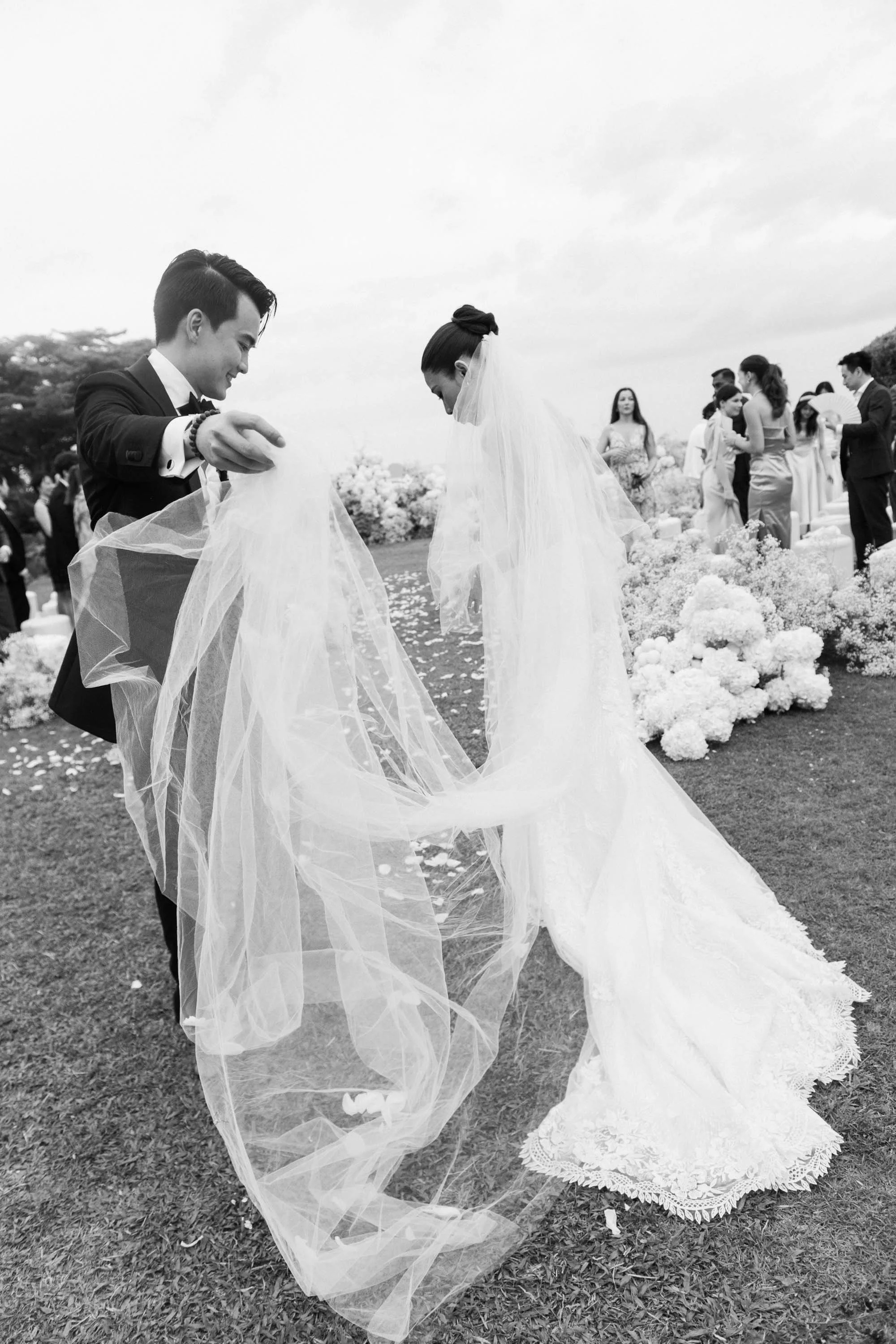 Groom adjusting the bride’s veil in the ocean breeze.