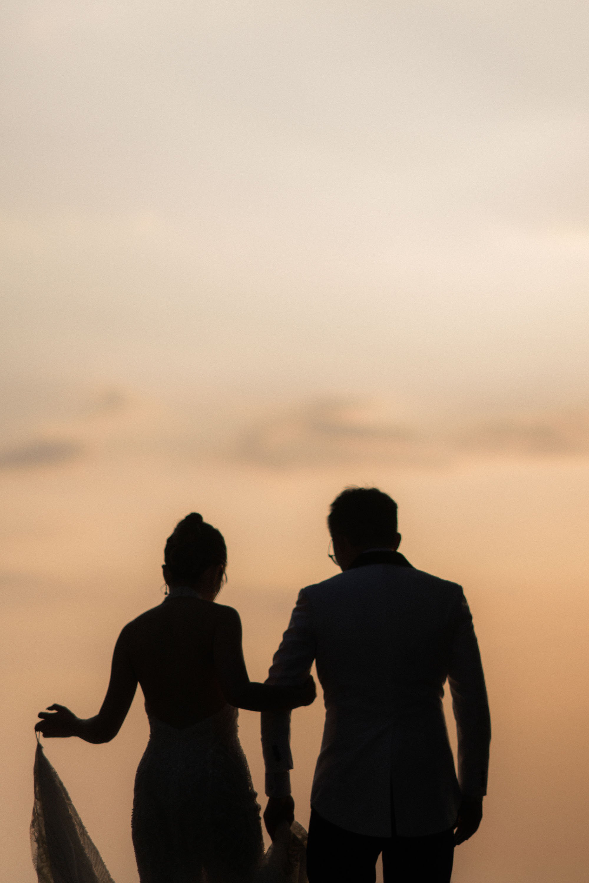Bride and groom walking toward the beach at sunset.