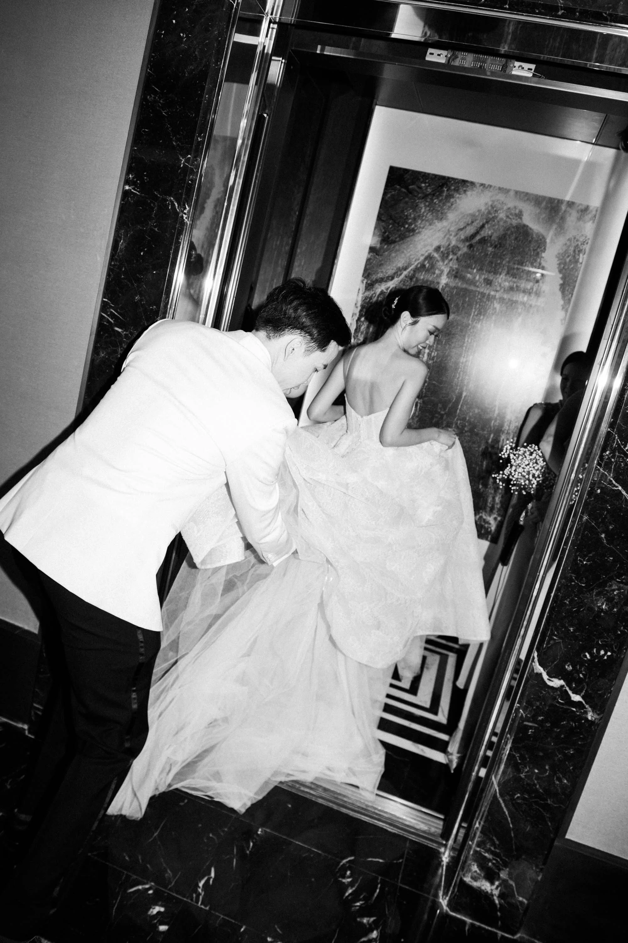Groom helping the bride with her wedding dress before entering the elevator.