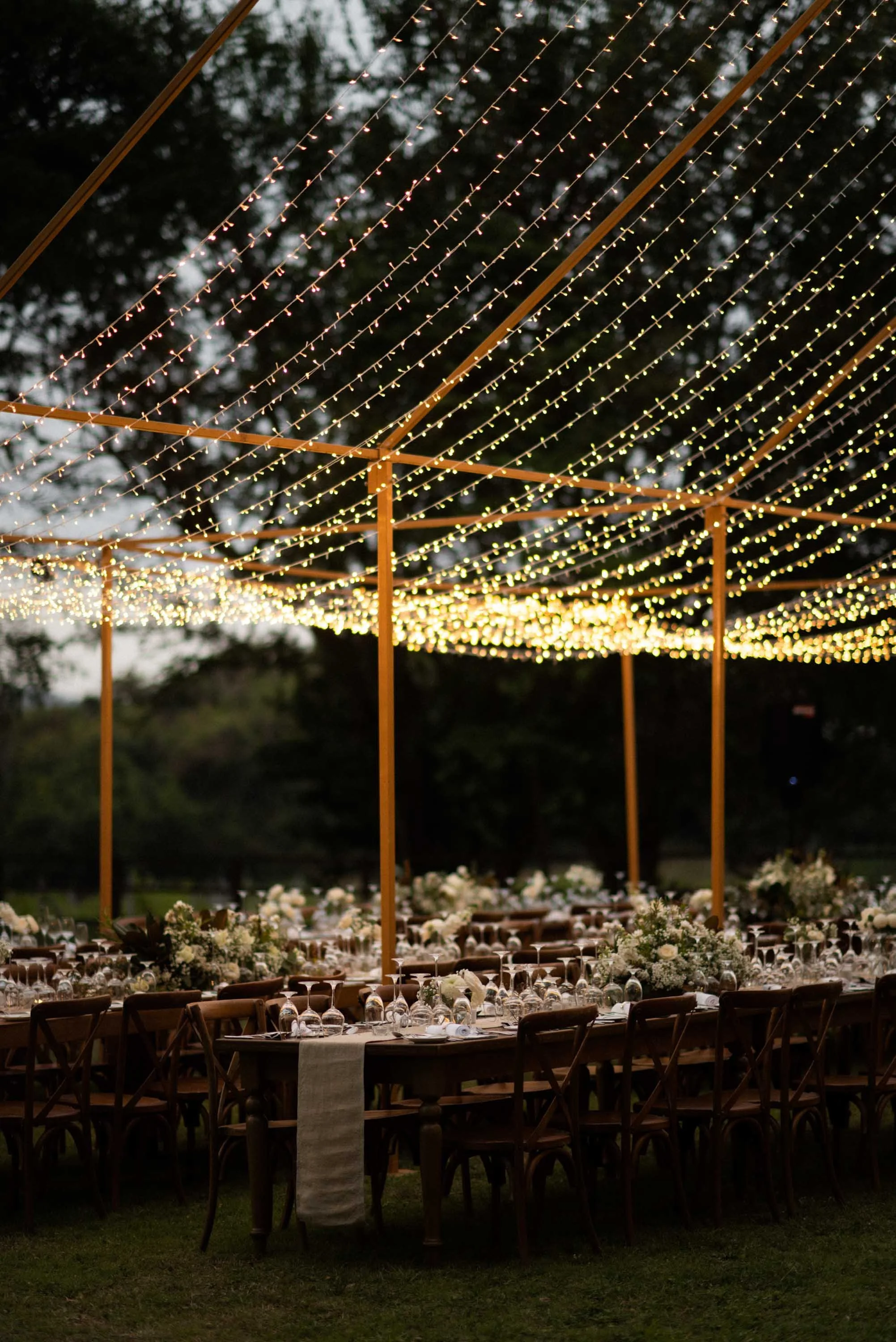 Dinner table decorated with flowers and string lights surrounded by nature.