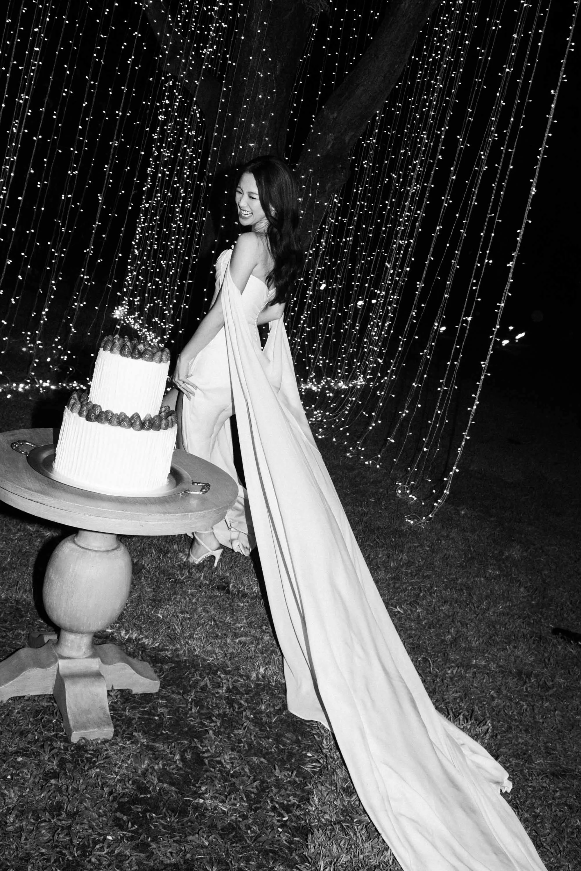 Bride walking toward the wedding cake beneath the evening lights.