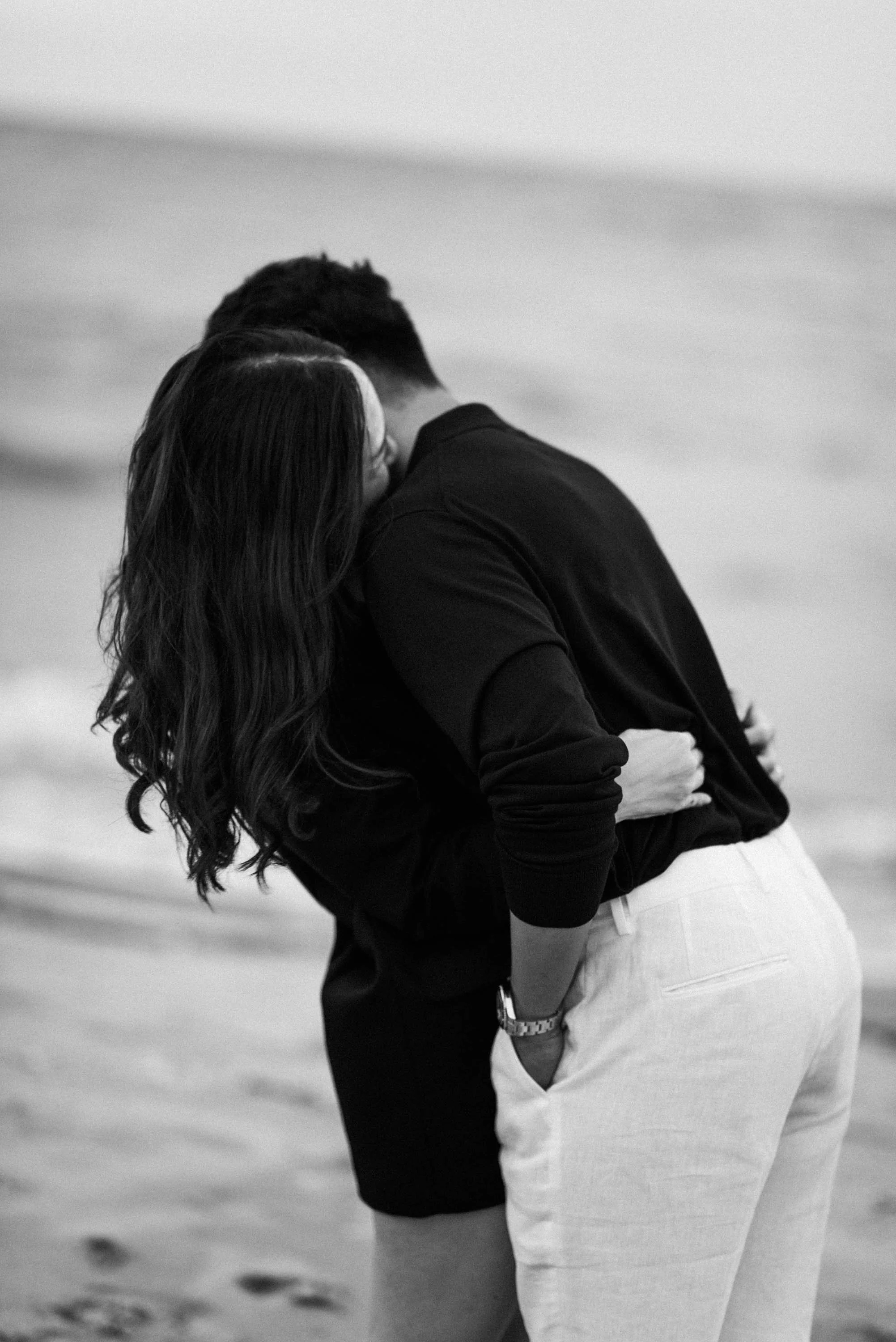 Man leaning back into his partner as she holds him by the beach.