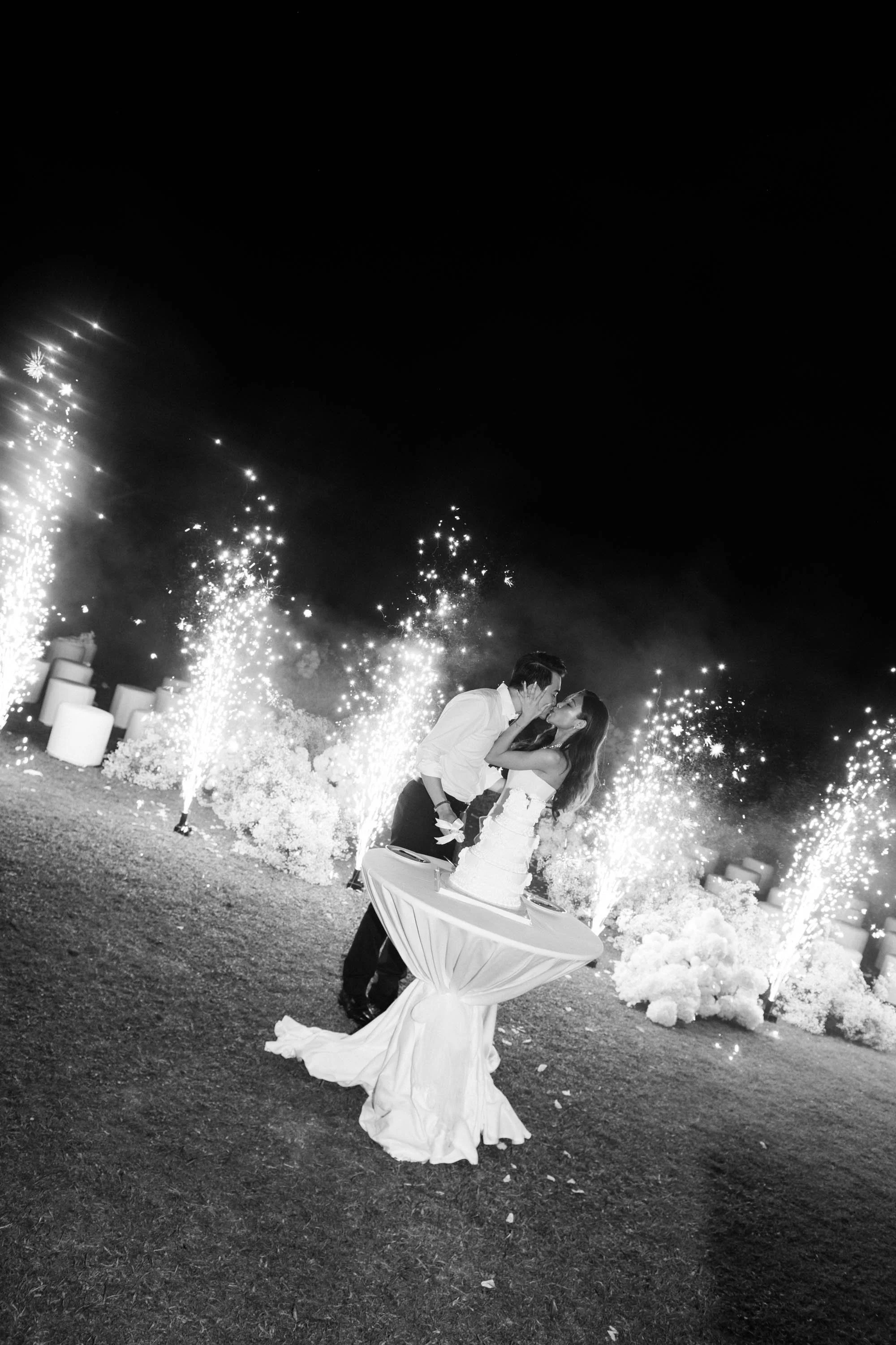 Bride and groom sharing a kiss with sparklers after cutting the wedding cake.