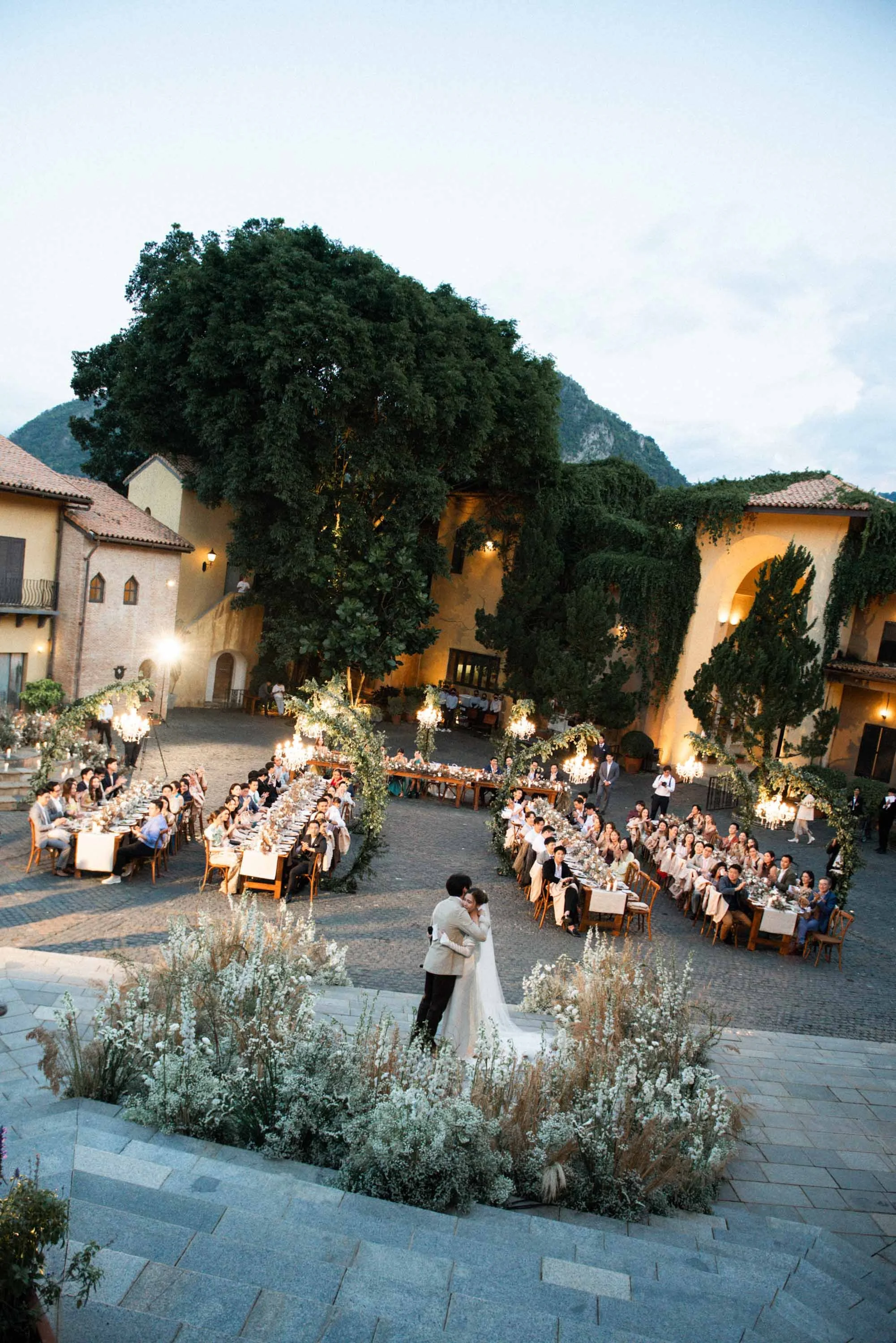 Bride and groom embracing after their vows with guests and the wedding setting in the evening light.