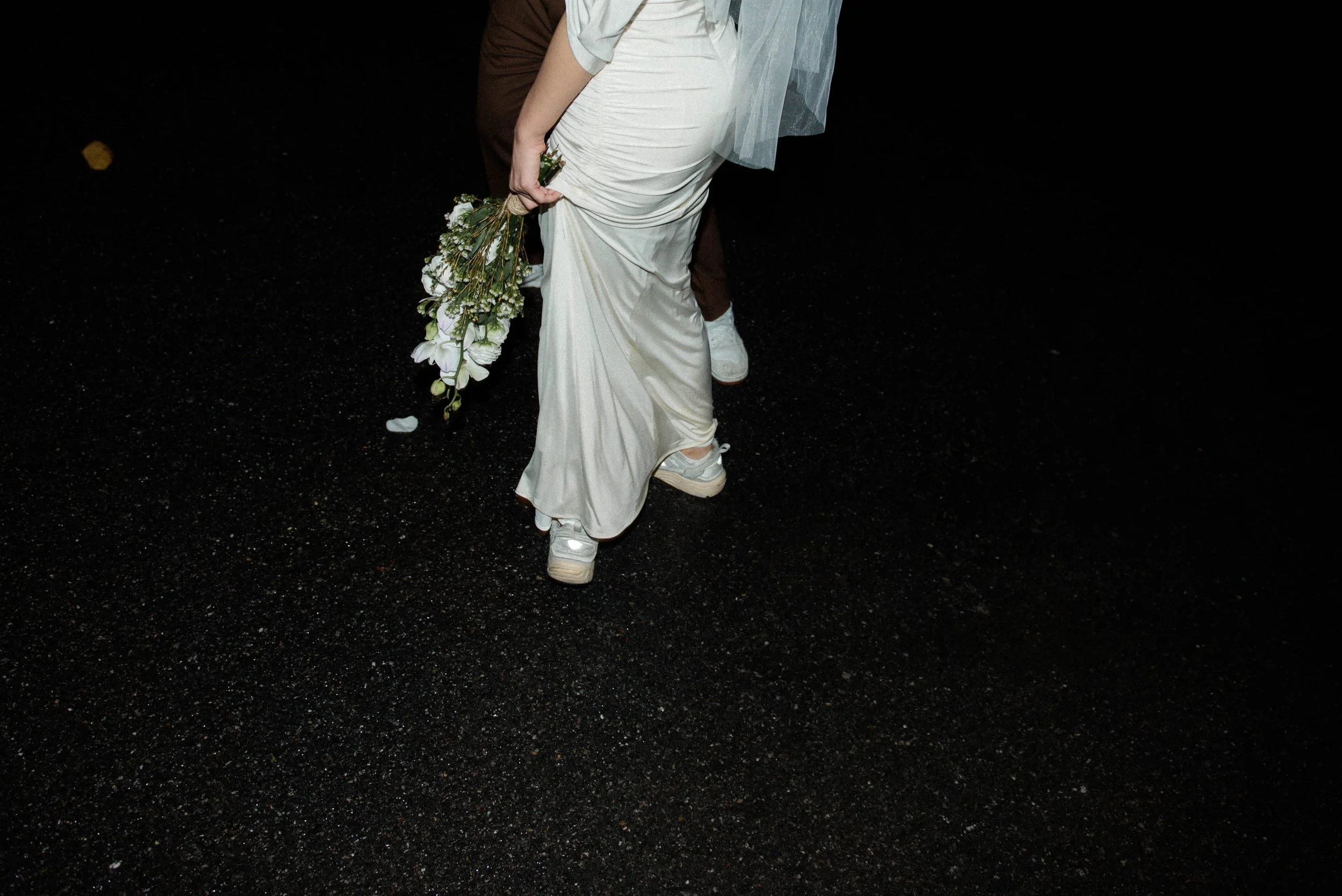 Close-up of the woman's hand holding her bouquet beside her wedding dress and shoes.