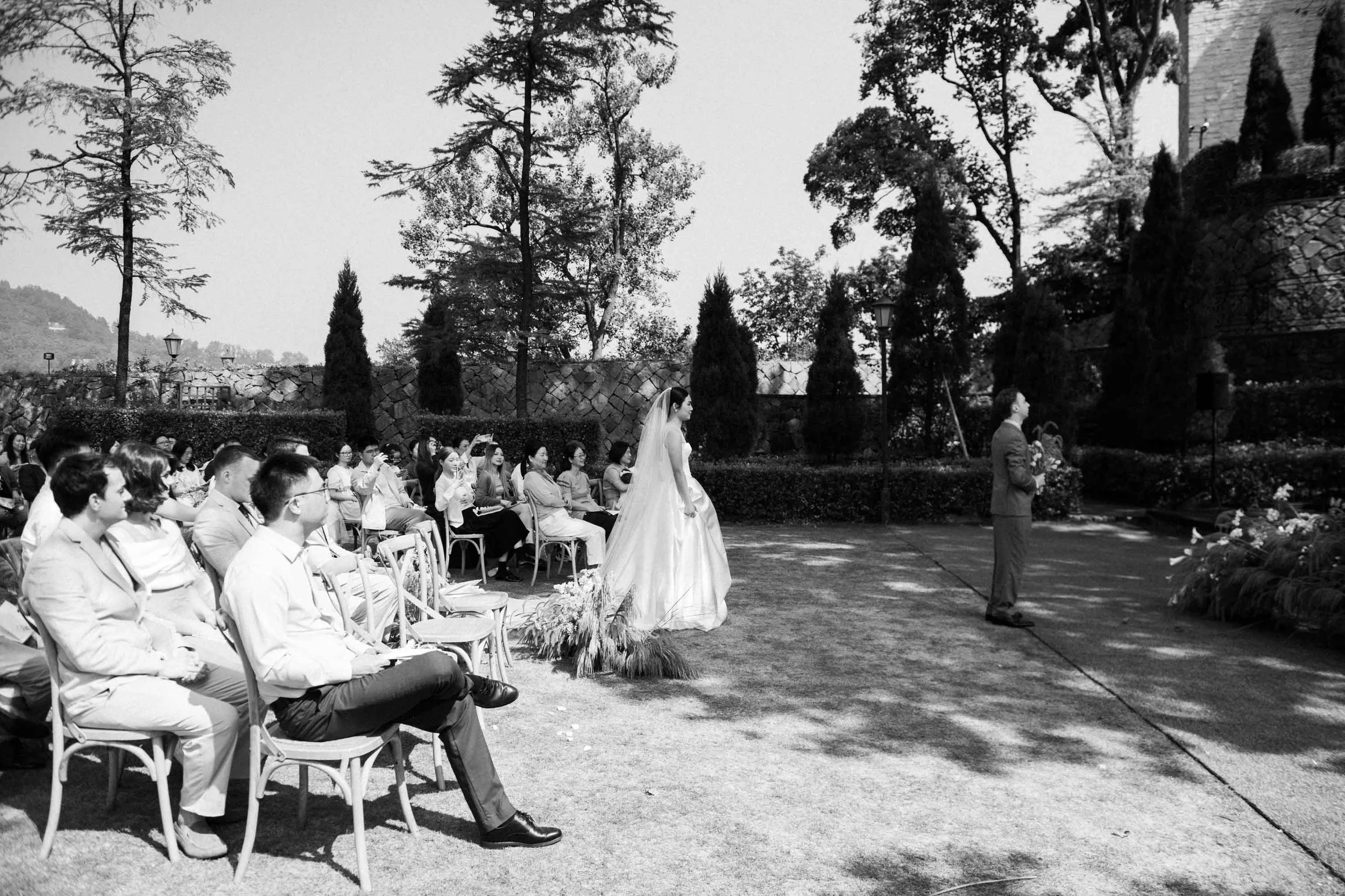 Bride arriving behind the groom as guests watch the ceremony begin.
