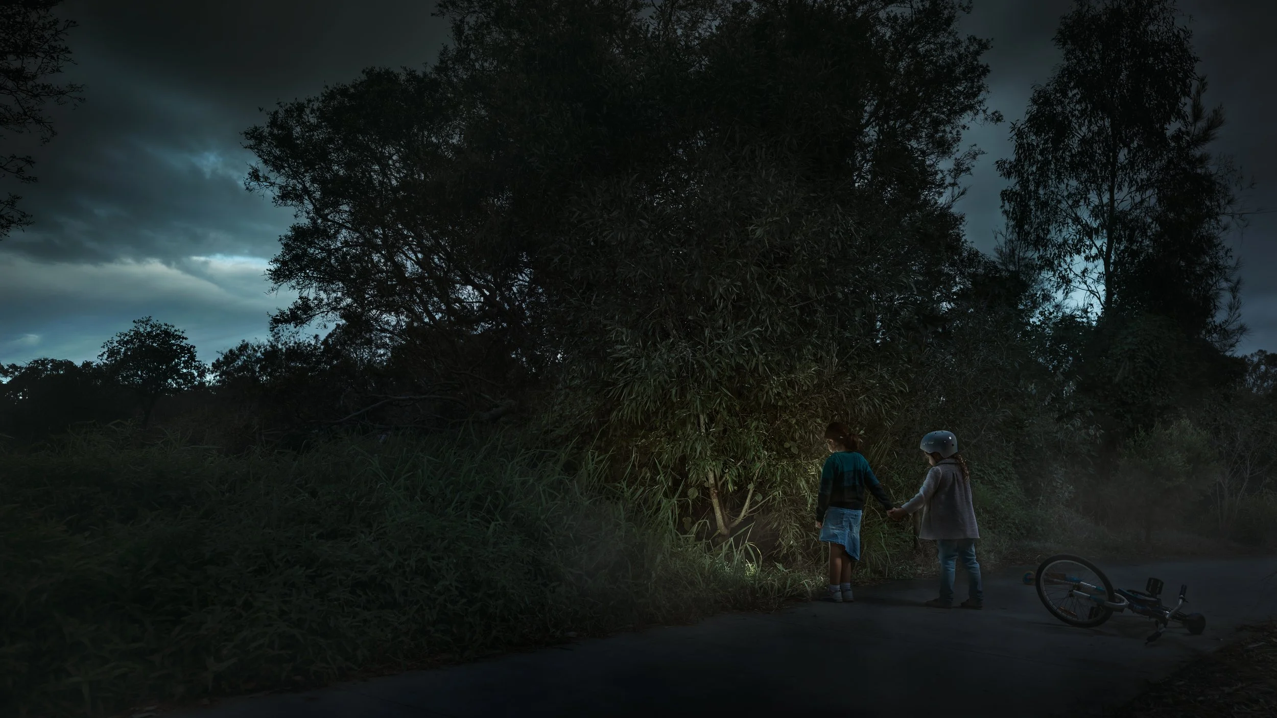 Cinematic fine art photography by Australian artist Alex Wright showing two children at dusk beside a fallen bicycle, exploring themes of innocence, mystery, childhood, curiosity and psychological storytelling.
