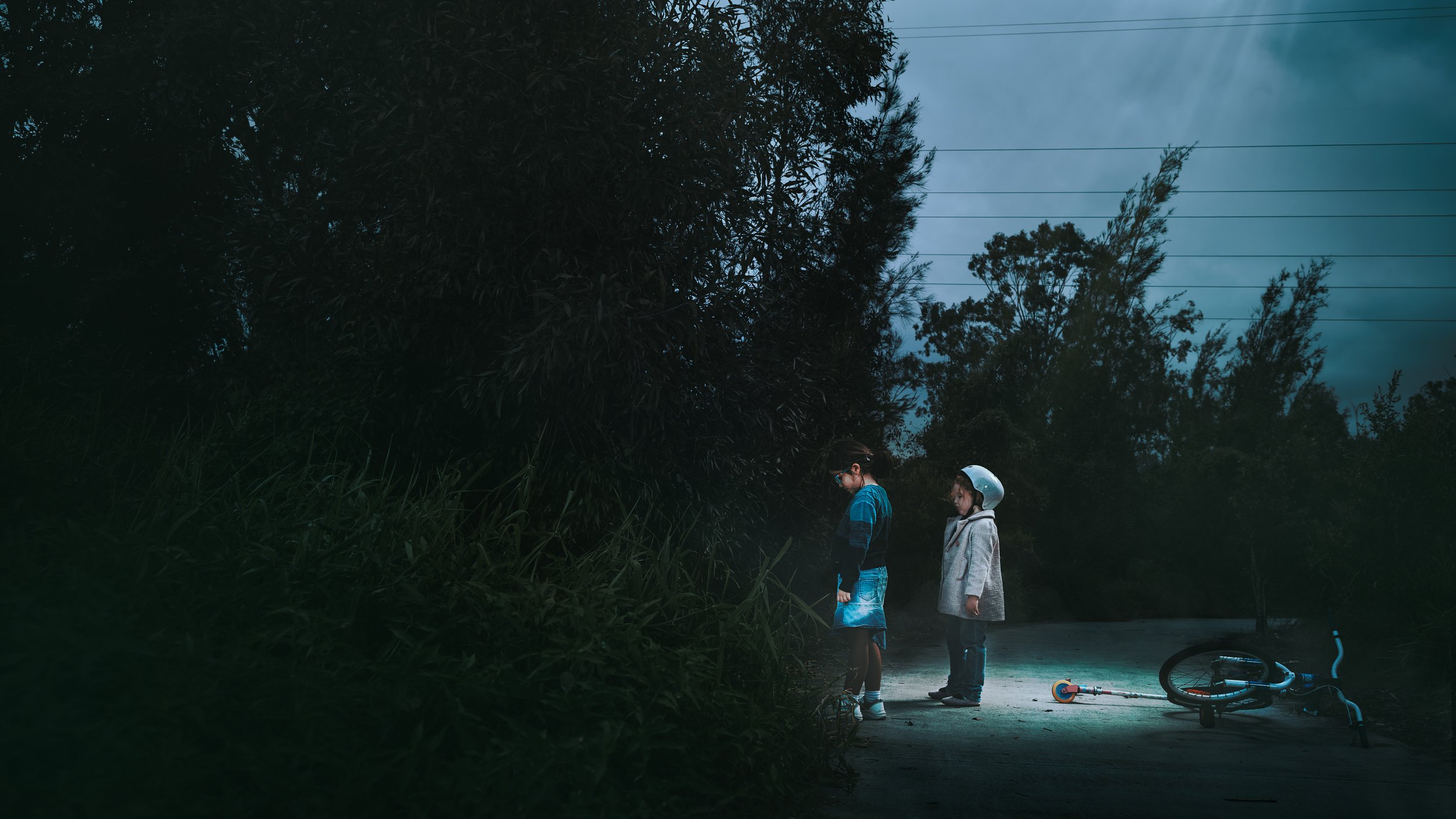 Cinematic fine art photography by Australian artist Alex Wright showing two children at dusk beside a fallen bicycle, exploring themes of innocence, mystery, childhood, curiosity and psychological storytelling.