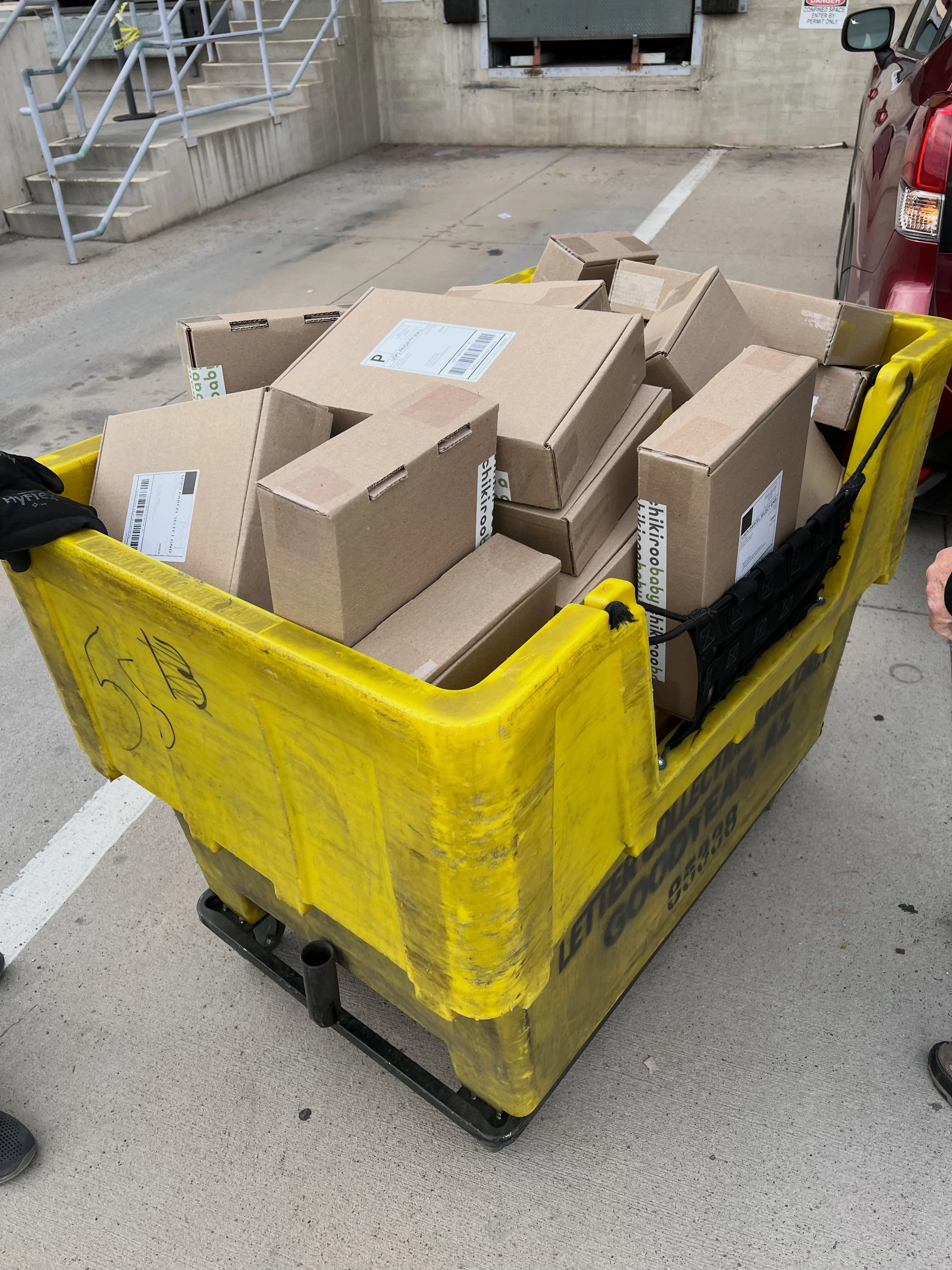 Yellow trash cart filled with cardboard boxes in a parking lot.