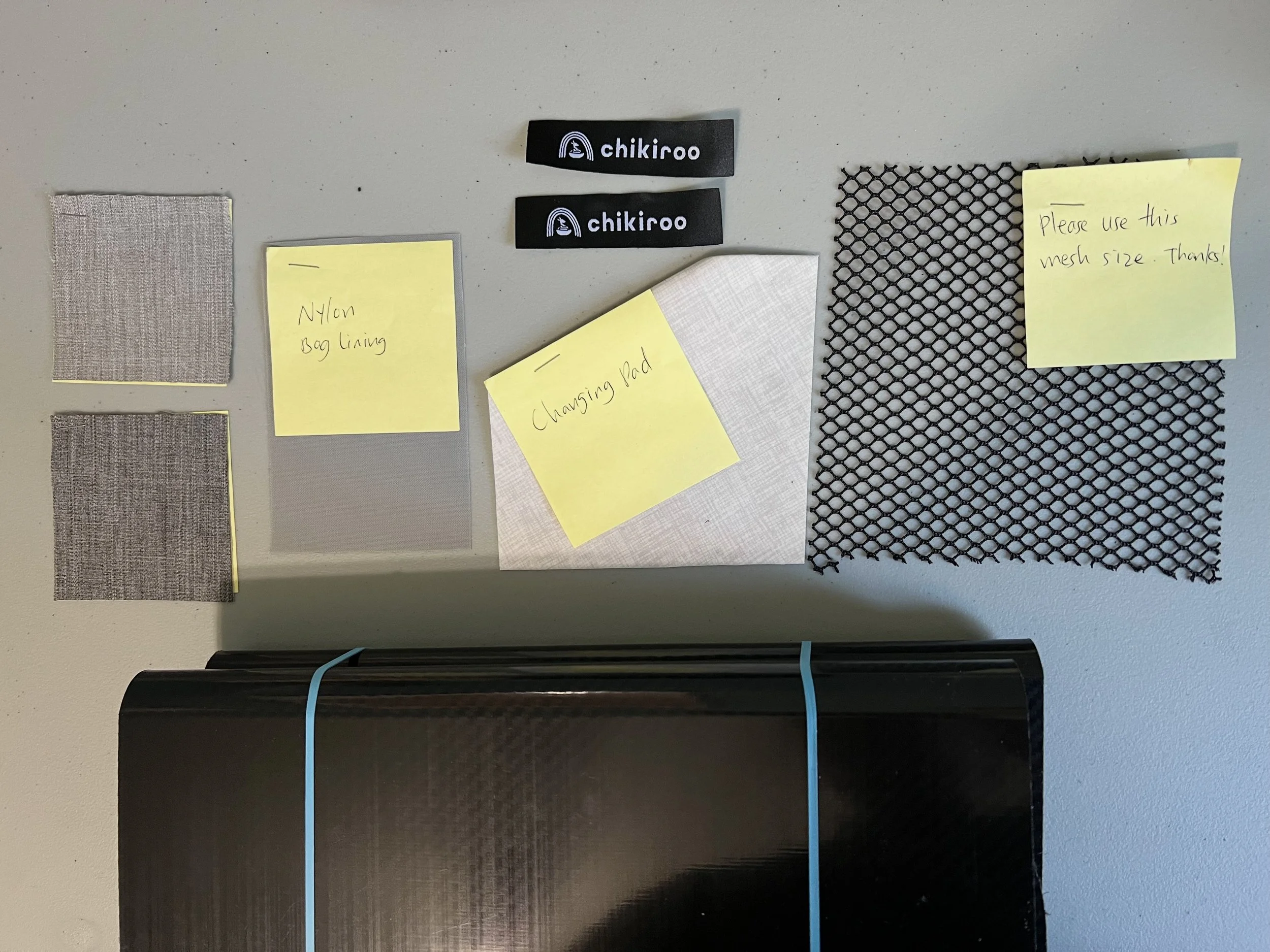Notification notes and various fabric swatches for project discussion, paired with the brand logo 'chikiroo' and a black mesh mesh sample, displayed on a light-colored table.