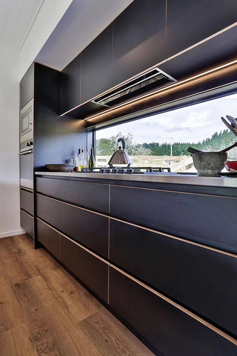 Dark handleless kitchen cabinetry with integrated lighting and wide picture window.