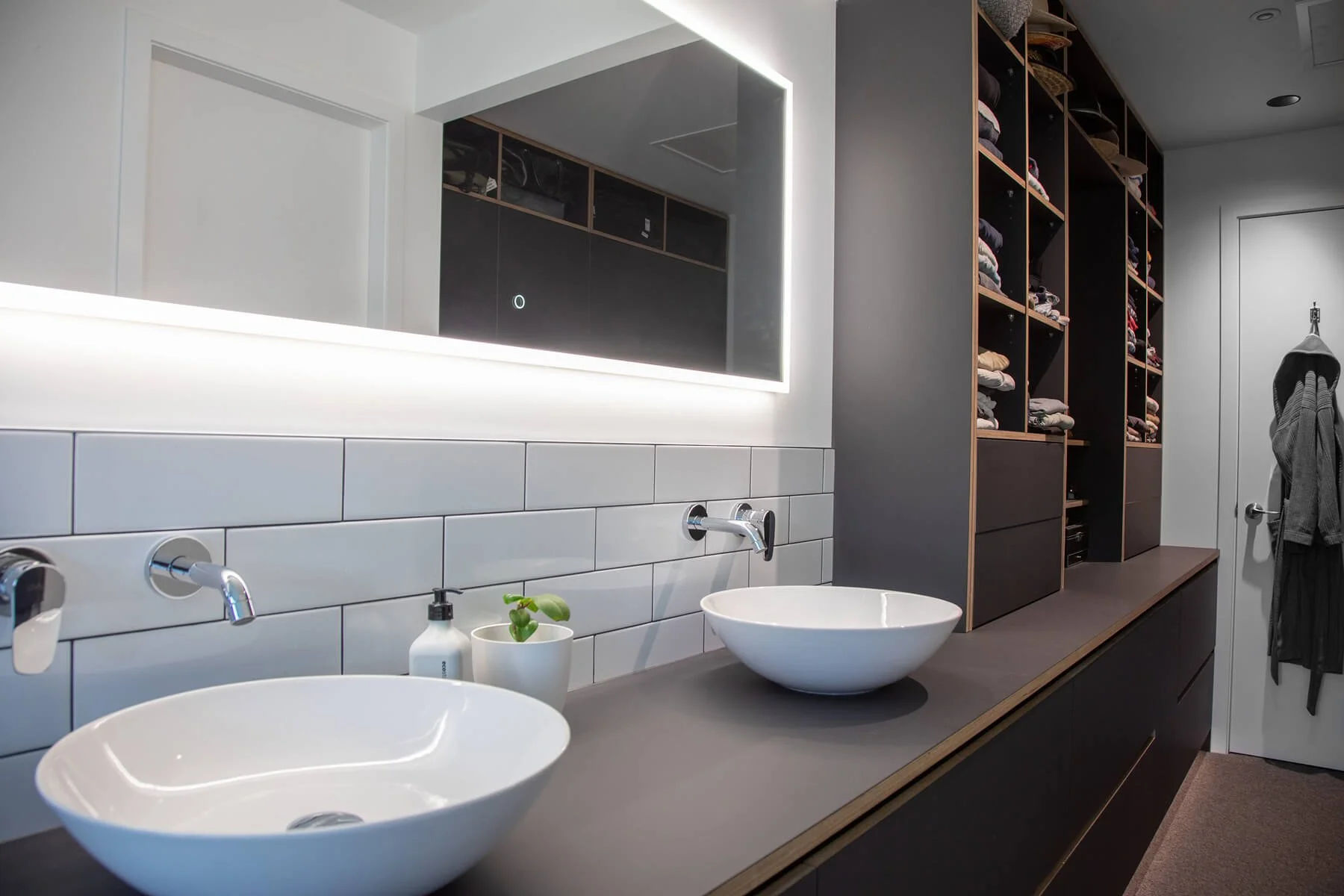 Dark double bathroom vanity with vessel basins, illuminated mirror and built-in wardrobe cabinetry.