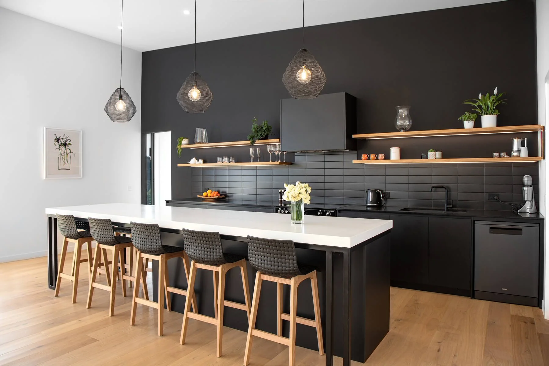 Contemporary black kitchen with long island, timber shelving and pendant lights.