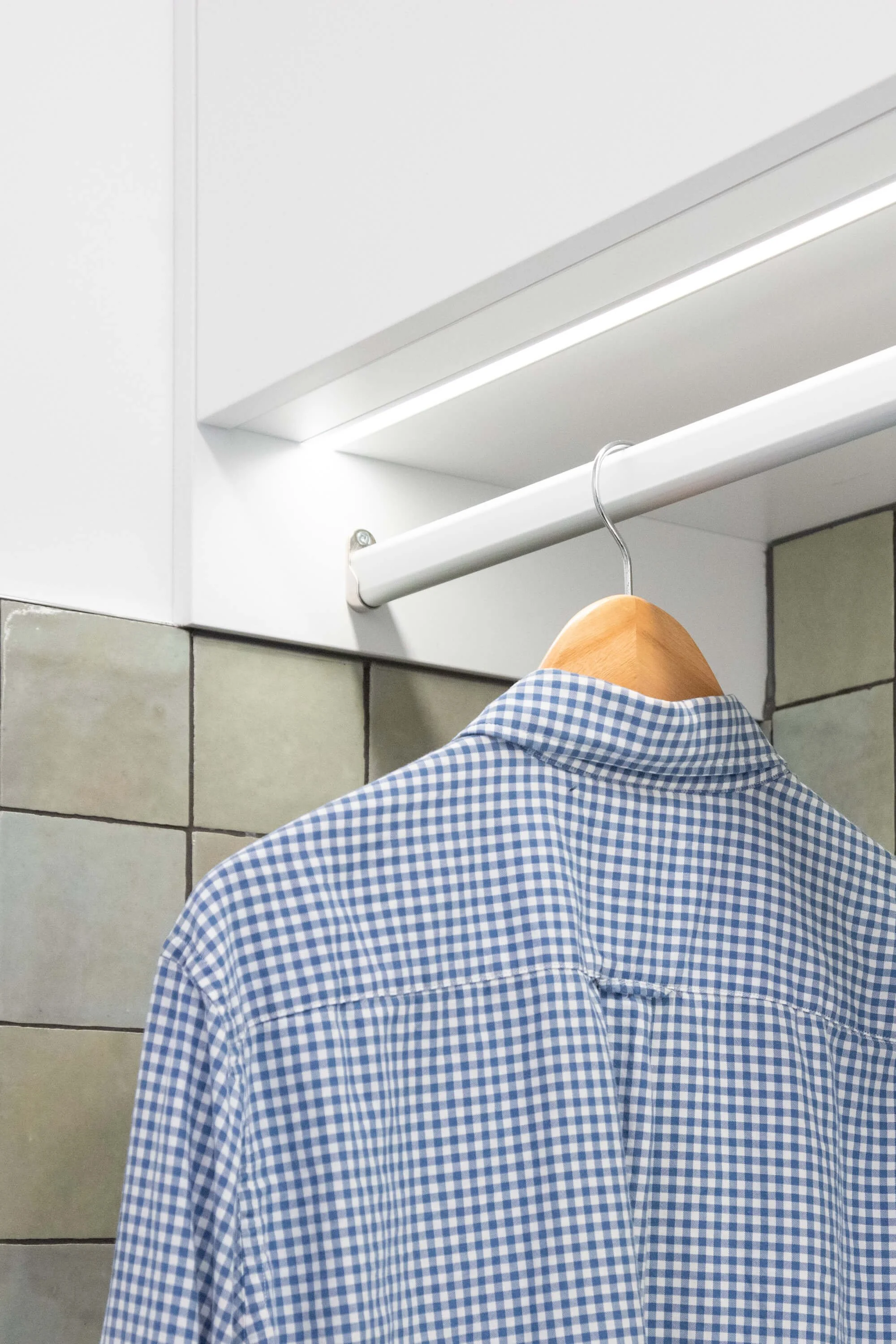 Hanging rail for shirts integrated into bespoke laundry cabinetry.
