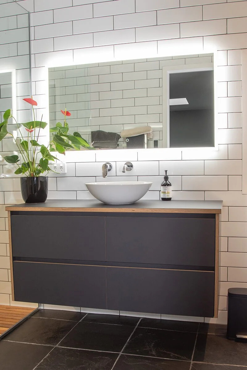Dark floating bathroom vanity with timber detailing, vessel basin and illuminated mirror.