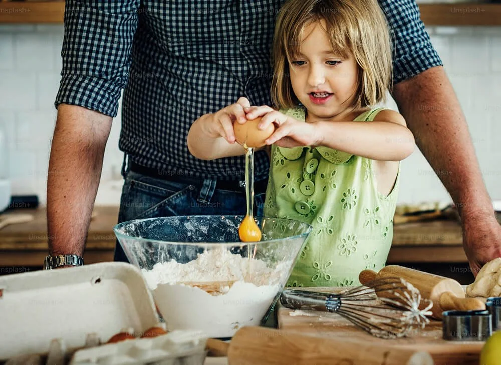 Child cracking an egg into a mixing bowl while baking in the kitchen.