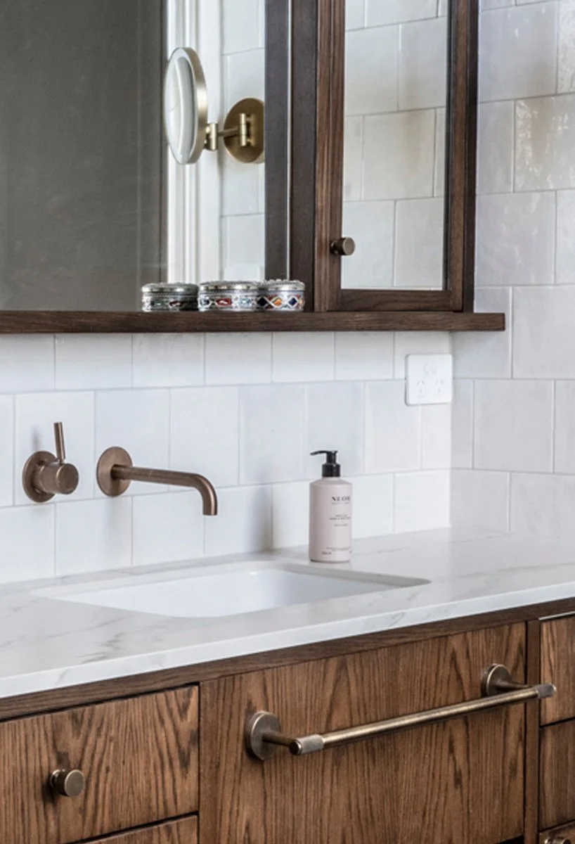 Close-up of timber bathroom cabinetry with white basin, wall-mounted brass tap and mirrored cabinet.