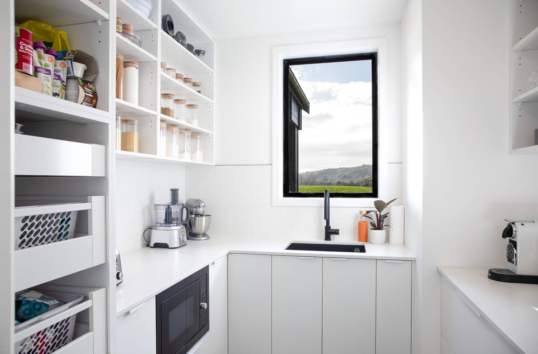 White scullery with open pantry storage and window overlooking the countryside.