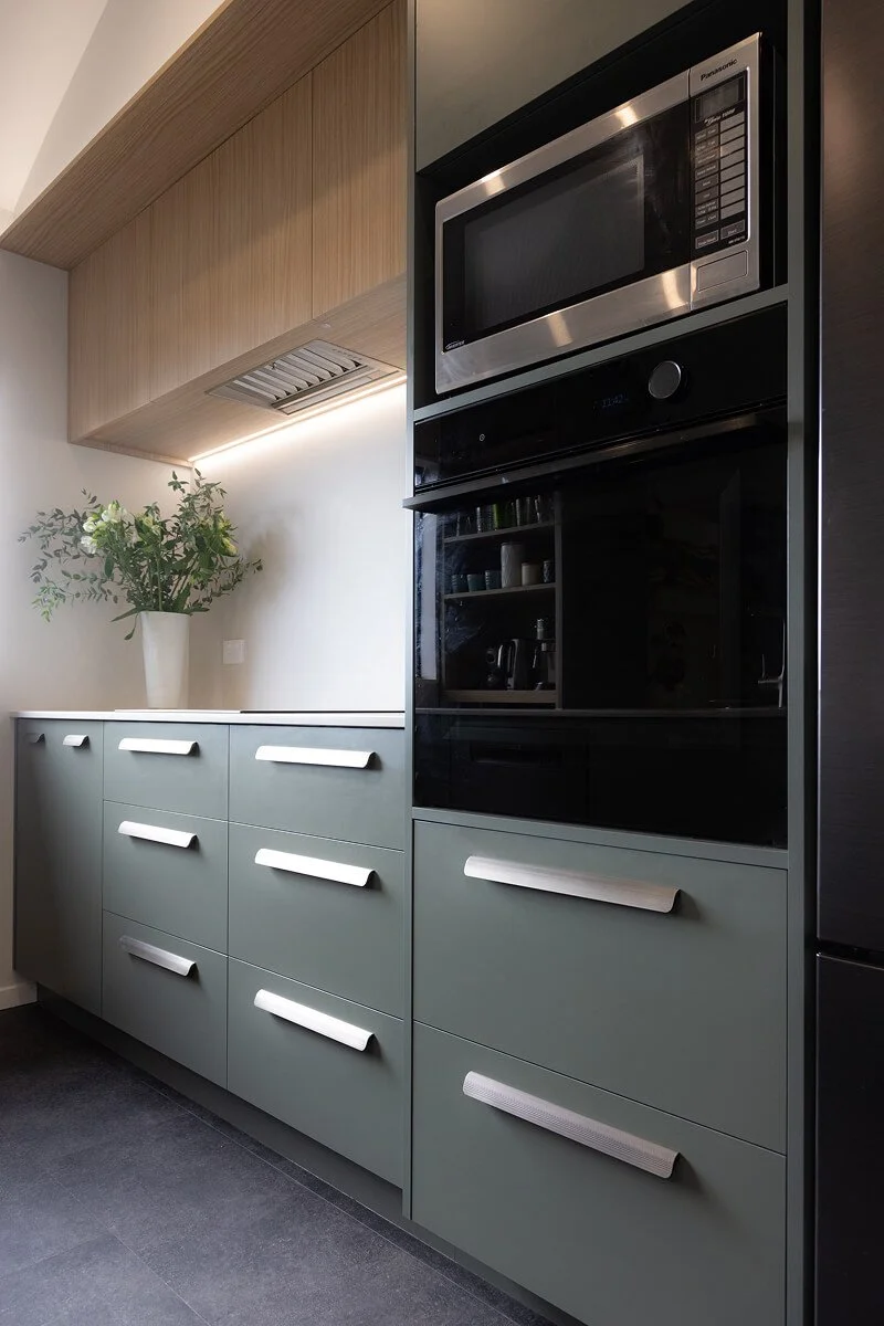 Sage green kitchen cabinetry with integrated appliances and brushed metal handles.
