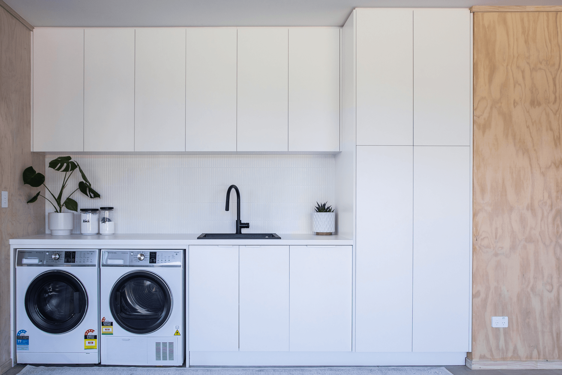 White laundry with full-height cabinetry, black sink and integrated washer and dryer.