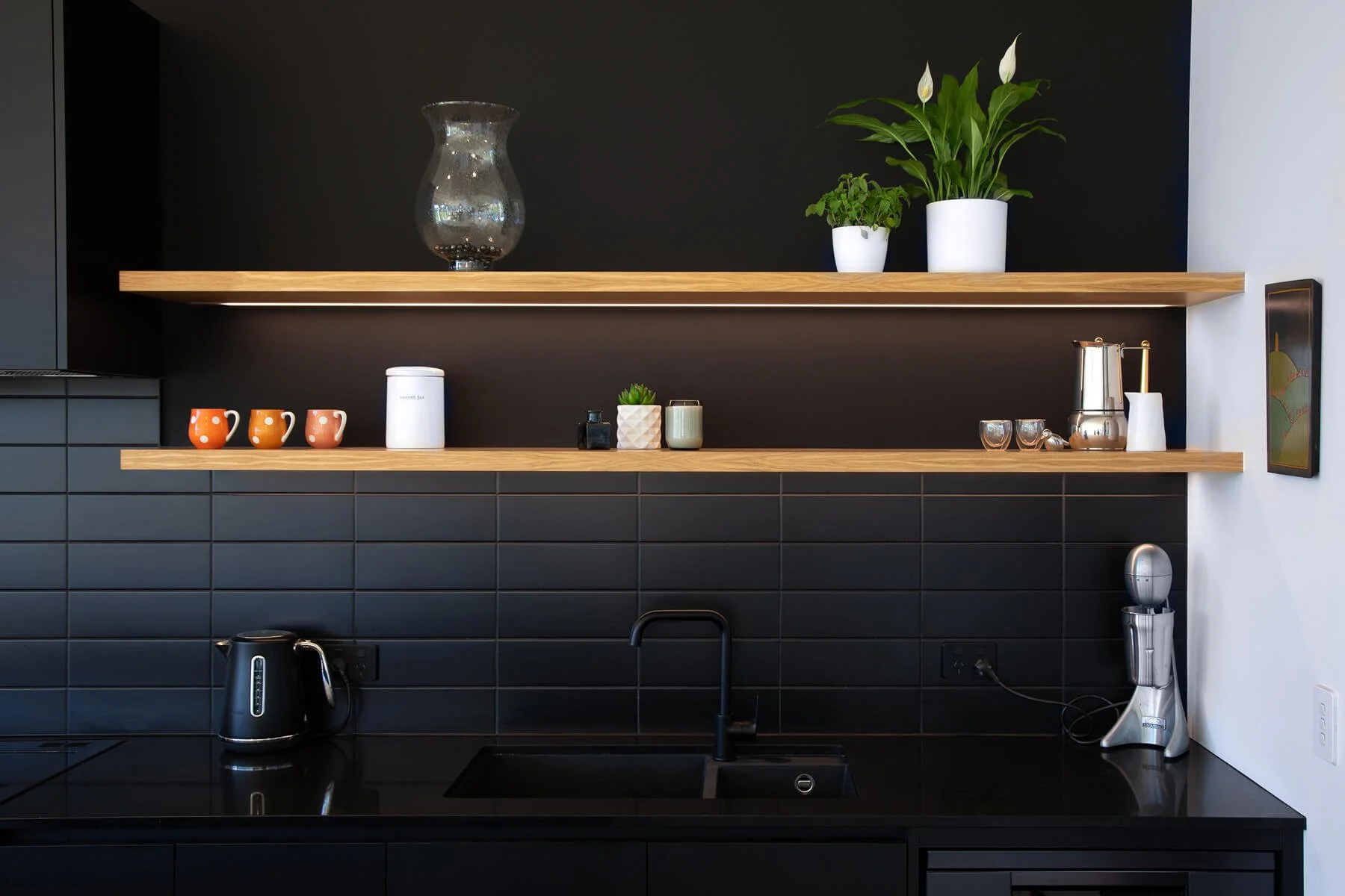 Black kitchen splashback with timber open shelving and integrated lighting.