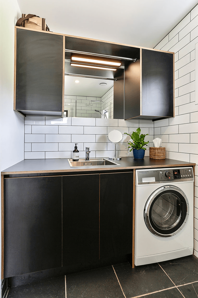 Compact laundry with dark cabinetry, stainless steel benchtop and integrated sink.