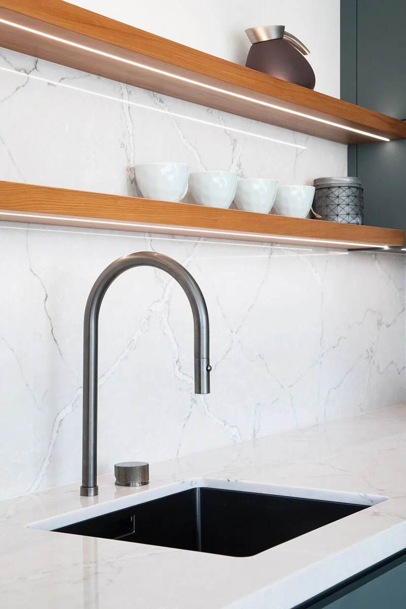 Kitchen sink with stone benchtop, timber shelving and integrated lighting.