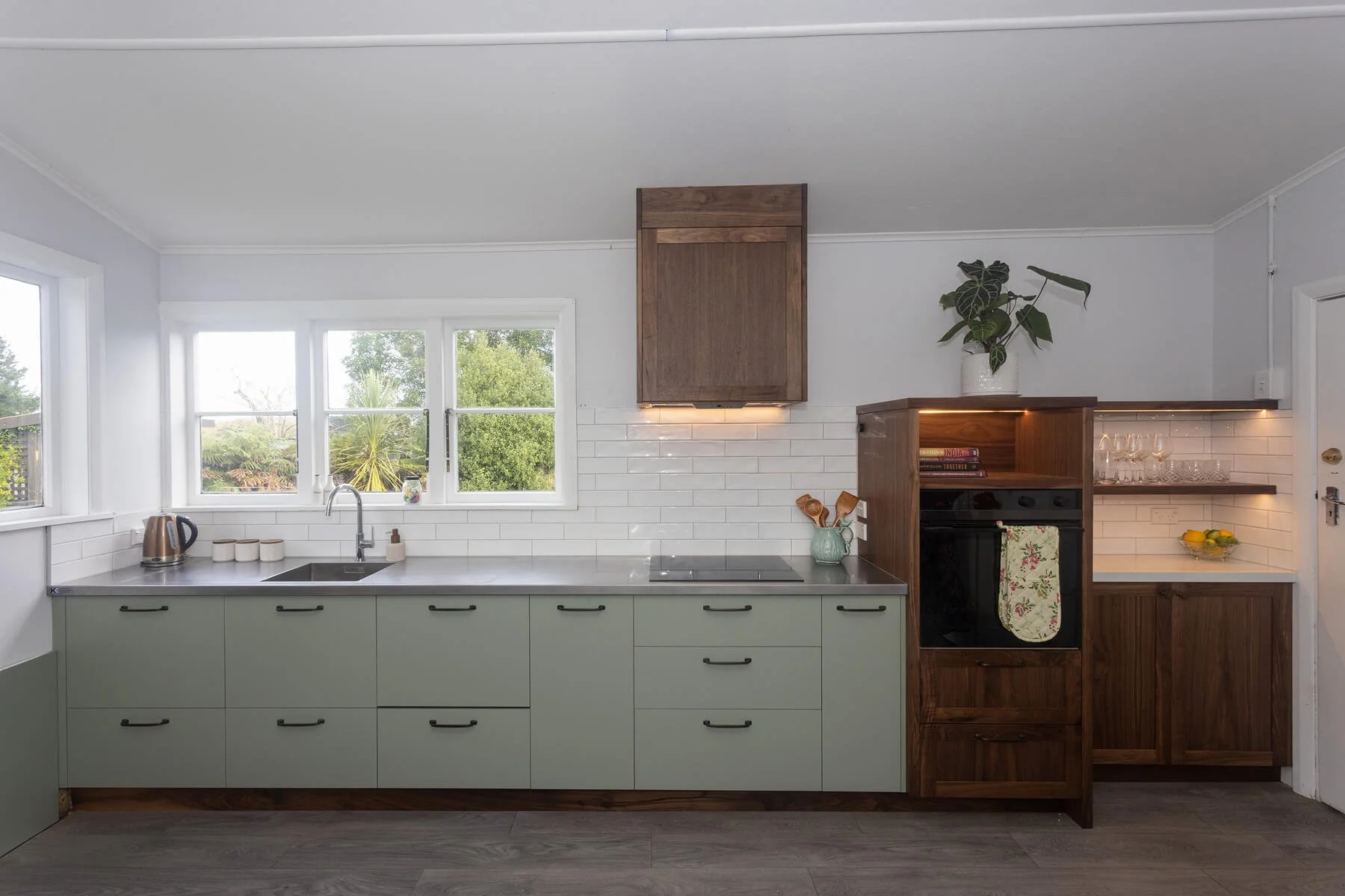 Sage green and walnut kitchen with generous drawers, sink and integrated appliances.