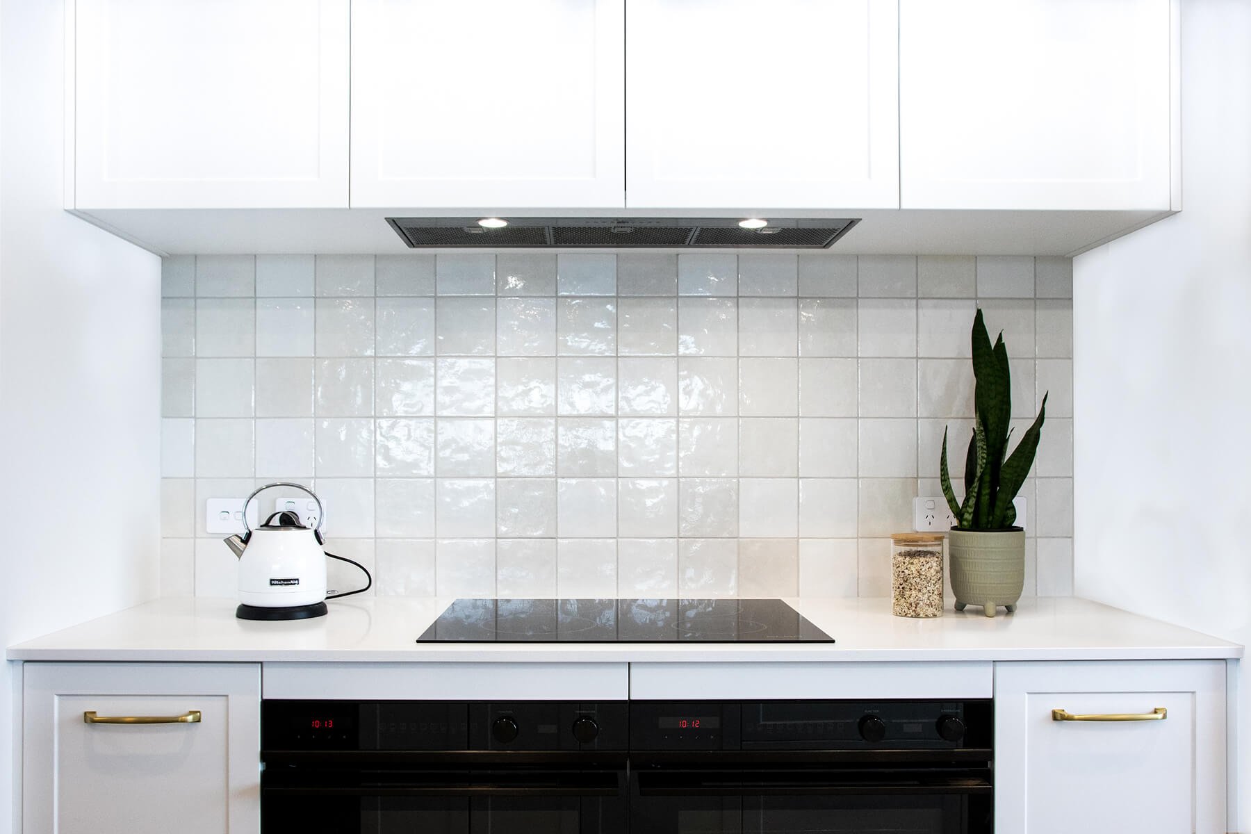 White kitchen with tiled splashback, induction cooktop and integrated ovens.