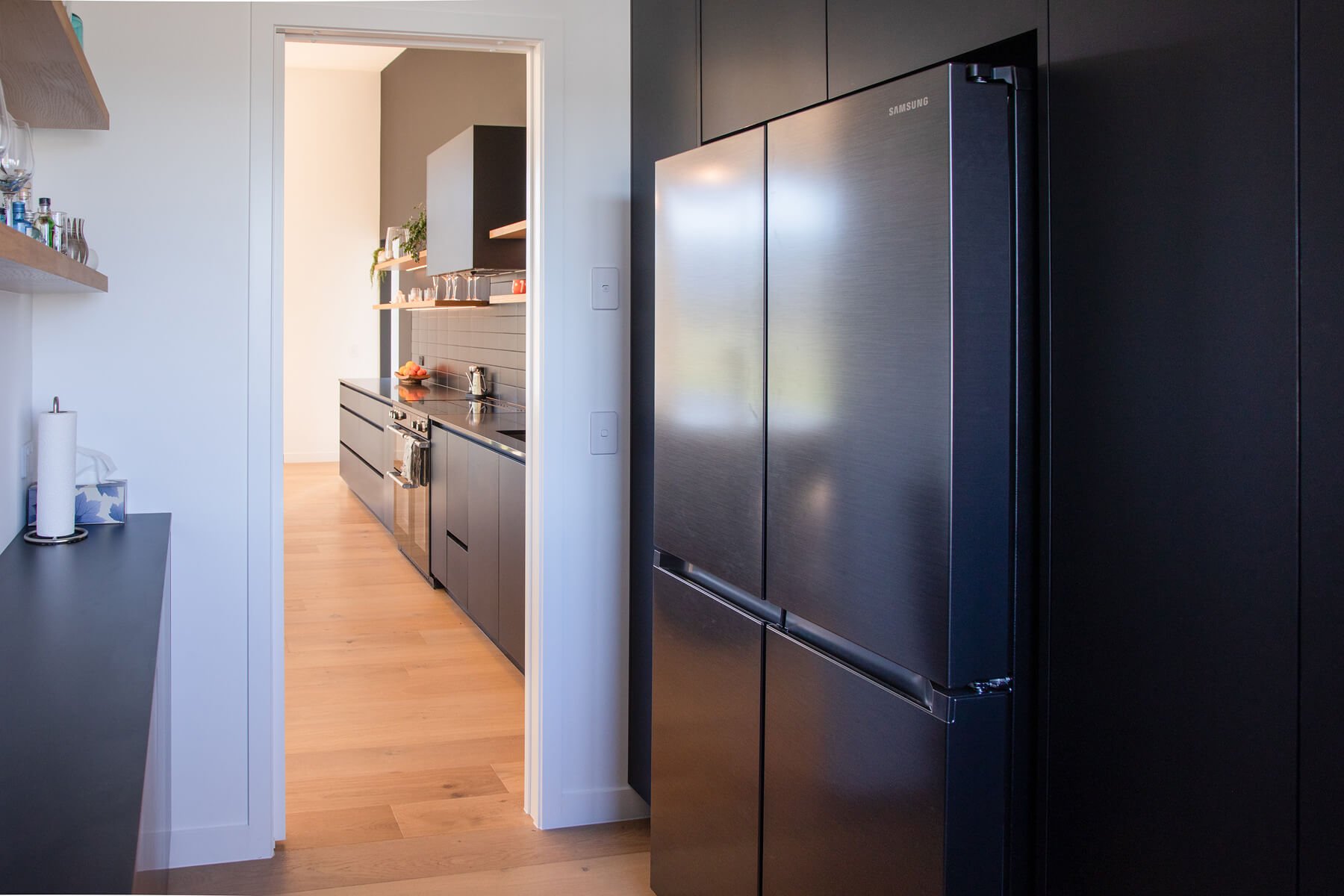 Integrated fridge within dark cabinetry beside the main kitchen.