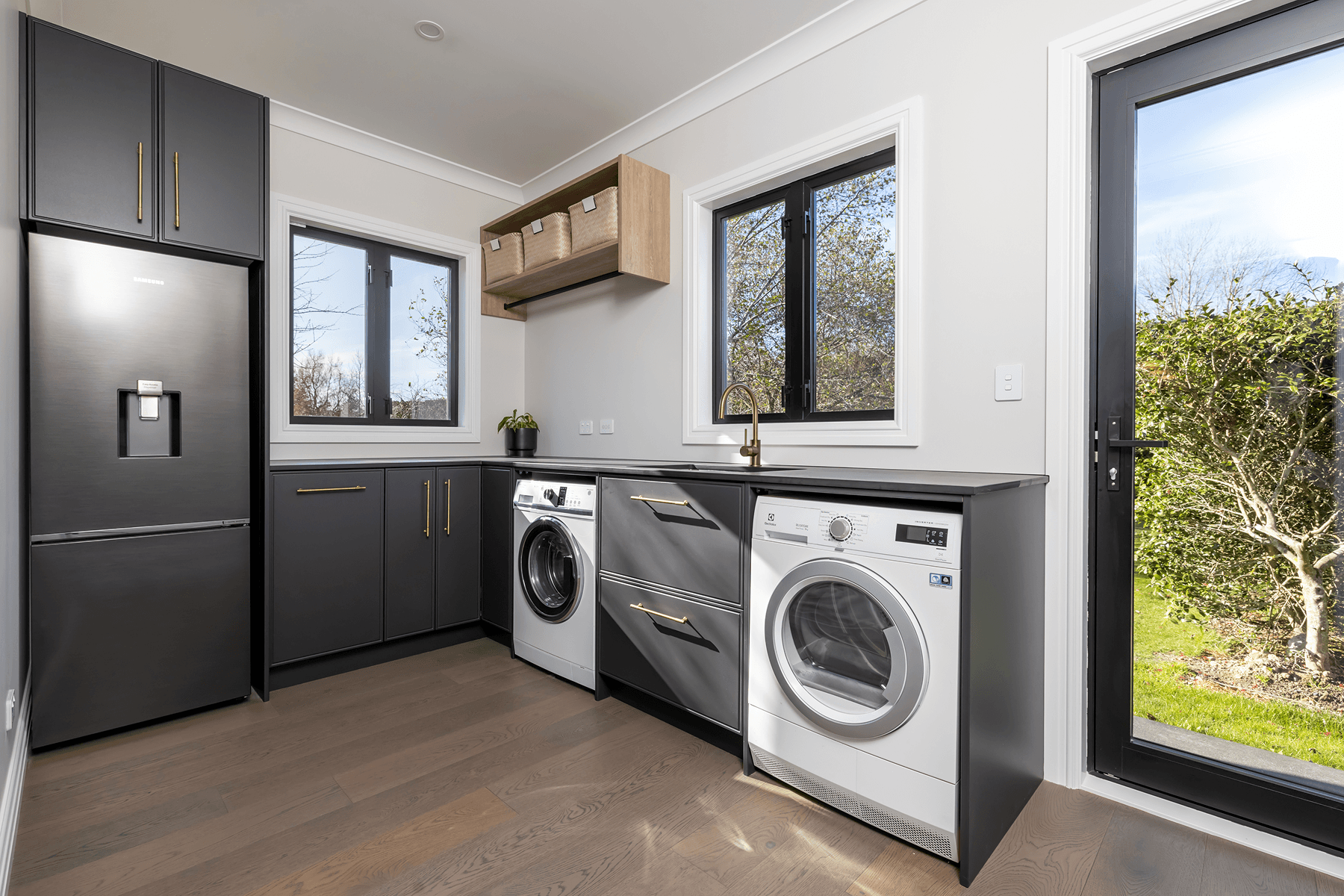 Dark laundry cabinetry with brass handles, washer, dryer and integrated storage.