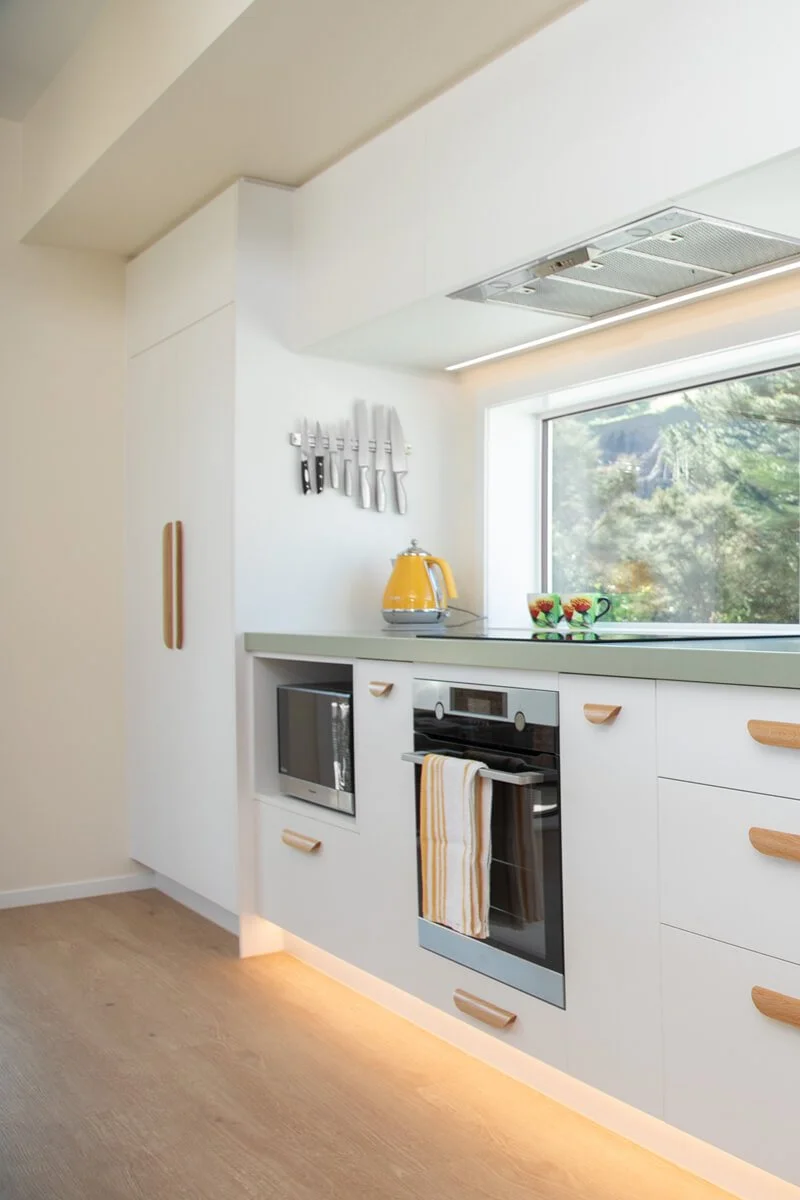 Light kitchen cabinetry with integrated appliances, timber handles and under-cabinet lighting.
