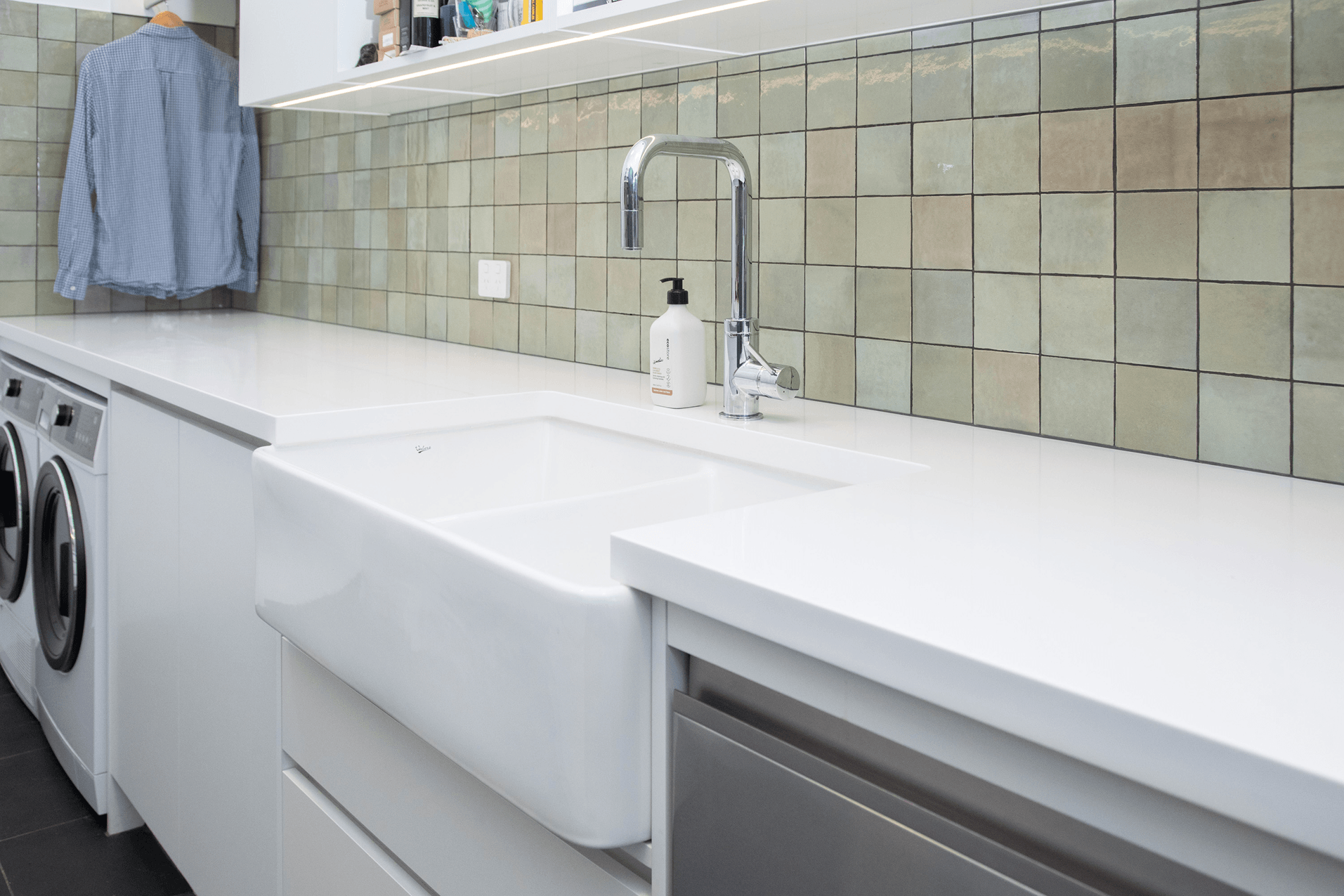 Deep laundry sink with white benchtop and green tiled splashback.