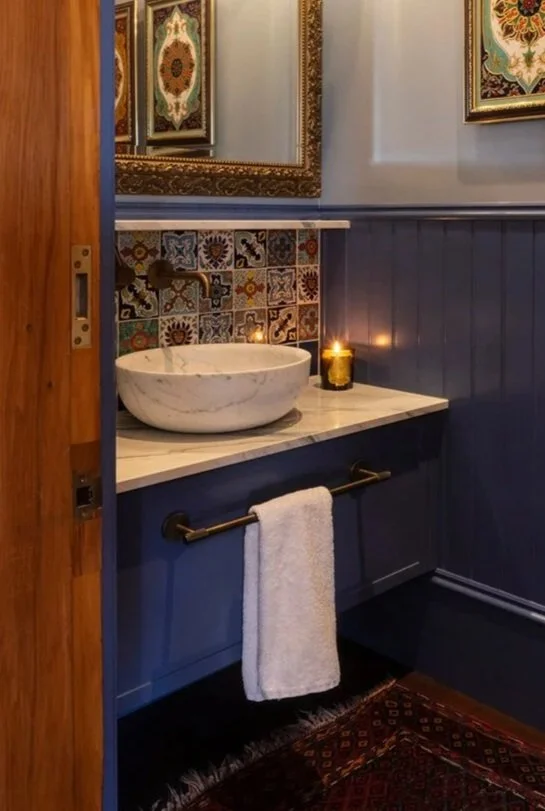 Blue bathroom vanity with marble vessel basin, brass fittings and patterned tile splashback.