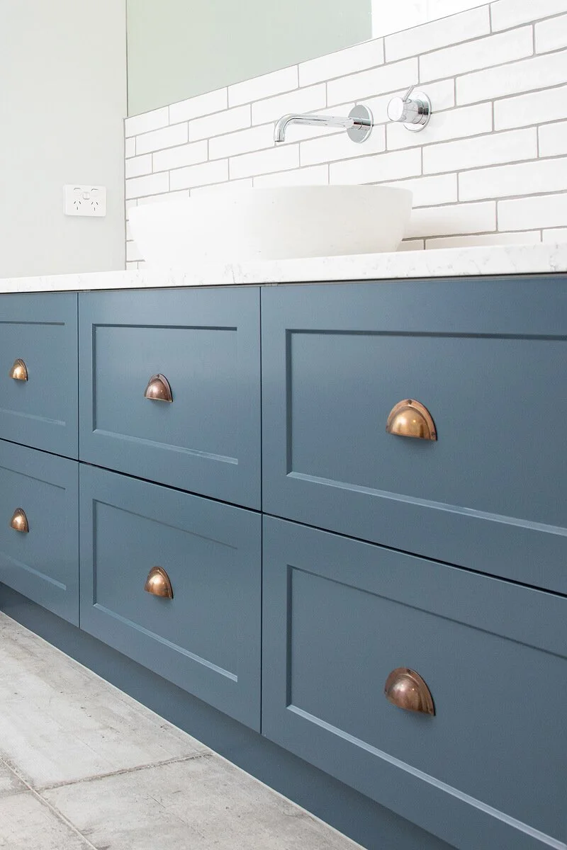 Close-up of blue vanity drawers with brass cup handles and vessel basin.