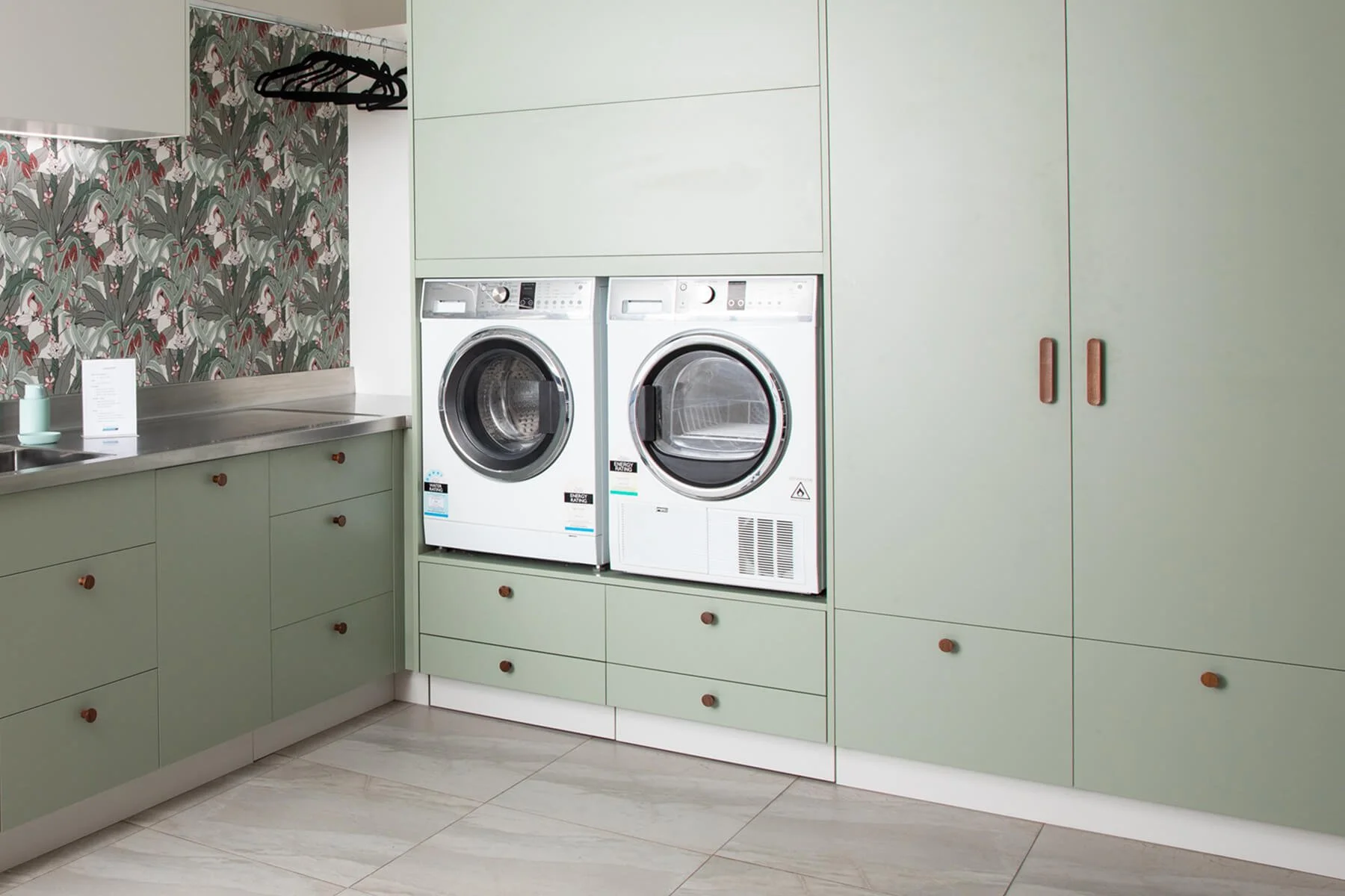 Bespoke laundry with sage green cabinetry and integrated washer and dryer.