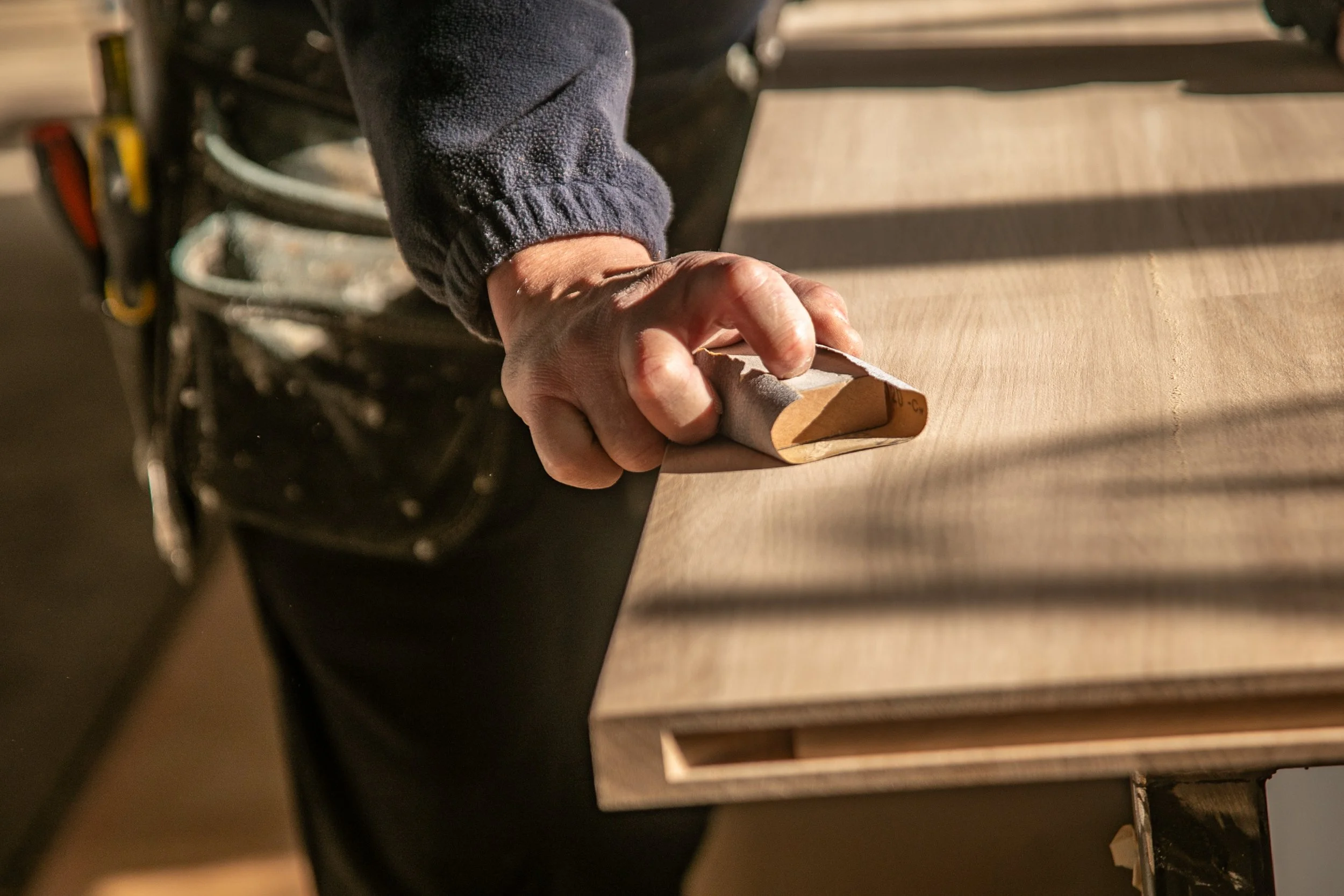 Carrolls craftsperson hand-sanding a timber panel in the workshop.