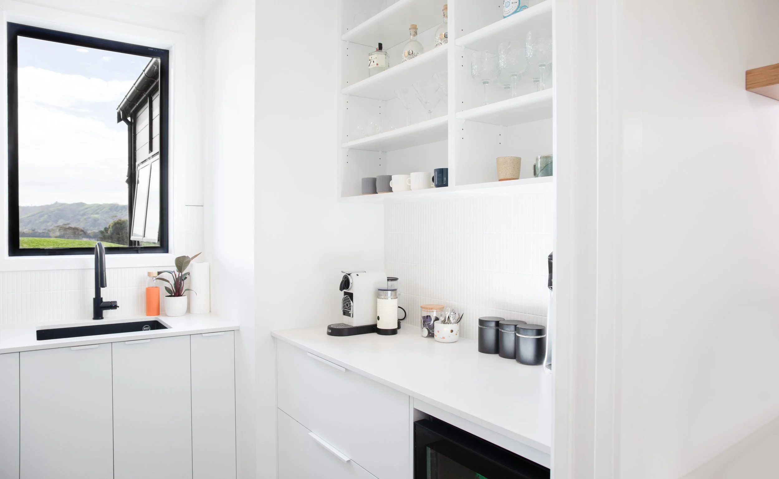 White scullery with open shelving, coffee station and built-in storage.
