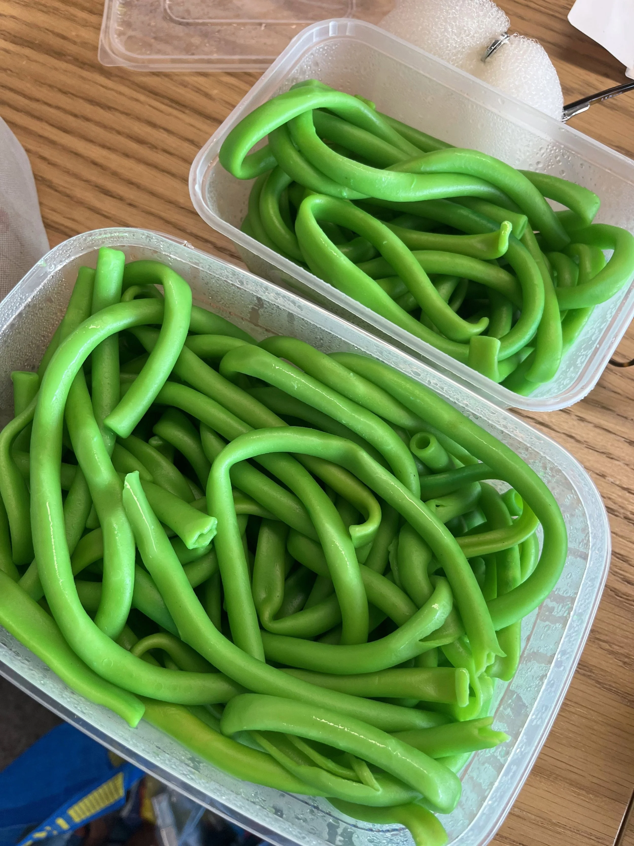 Two clear plastic containers filled with fresh, green, twisted green beans placed on a wooden surface.