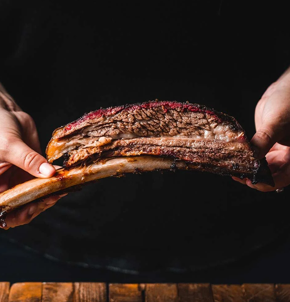 Person holding a large slab of cooked, smoked brisket with a smoky crust.