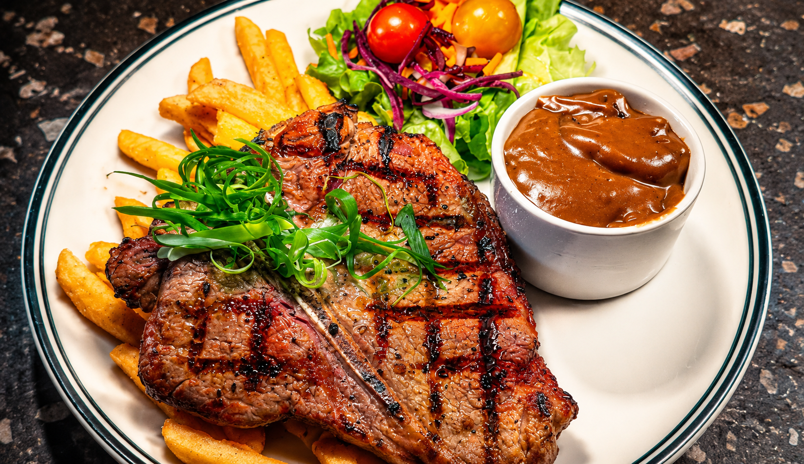 Grilled steak topped with green sprouts, served with French fries, side salad with cherry tomatoes, shredded purple cabbage, and lettuce, along with a cup of brown gravy on a white plate.