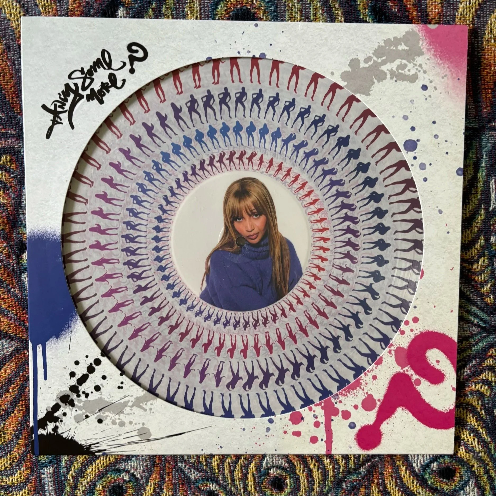 Graphic design book cover with a pattern of multicolored human silhouette figures forming concentric circles around a central photo of a woman with brown hair, wearing a blue turtleneck sweater, holding a microphone, against a decorated background with paint splatters and a handwritten phrase that says "Have some style, more?" in black cursive.