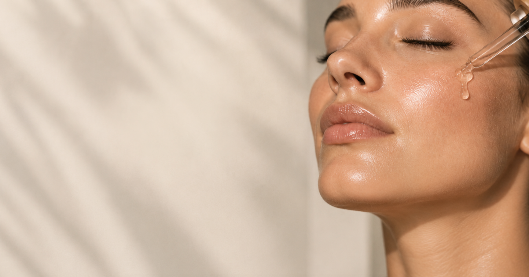 A woman receiving a facial treatment, with her eyes closed, as a skincare specialist applies serum with a dropper to her face.