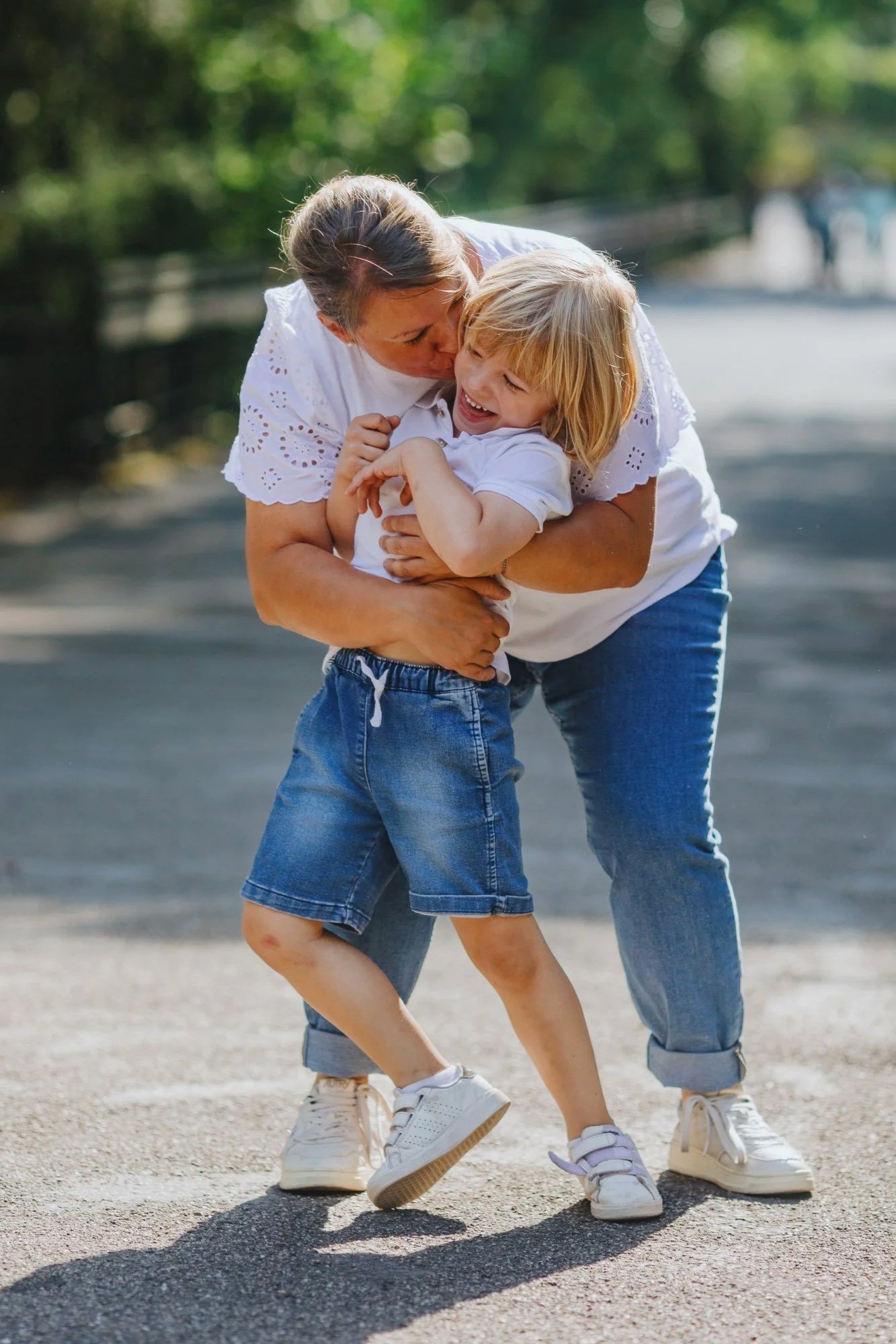 Eine Mutter umarmt ihr Kind, welches die Umarmung toll findet, aber auch gerne gleich weiter rennen würde.