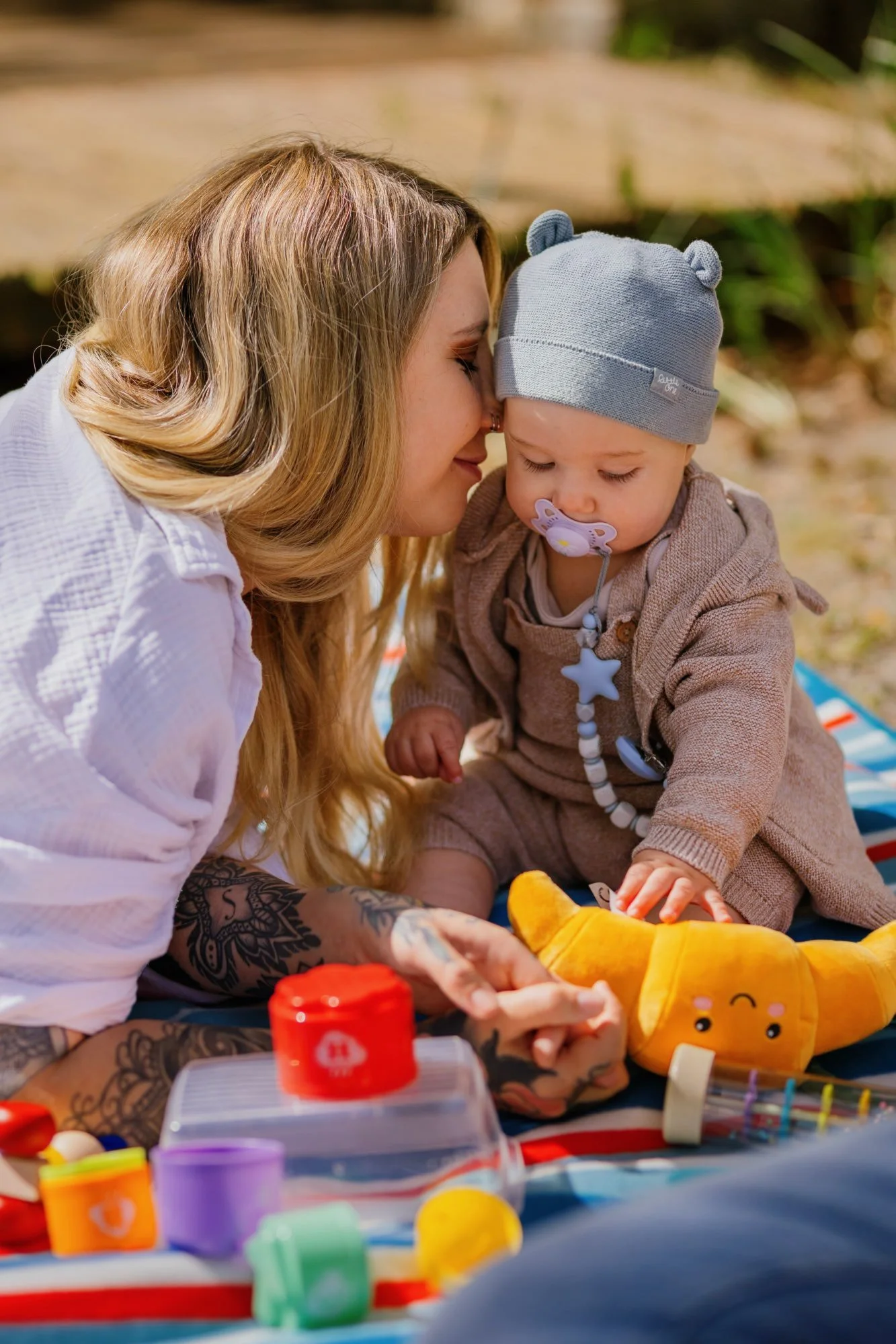Mutter schmust zärtlich mit ihrem Baby auf einer Picknickdecke im Sonnenlicht.