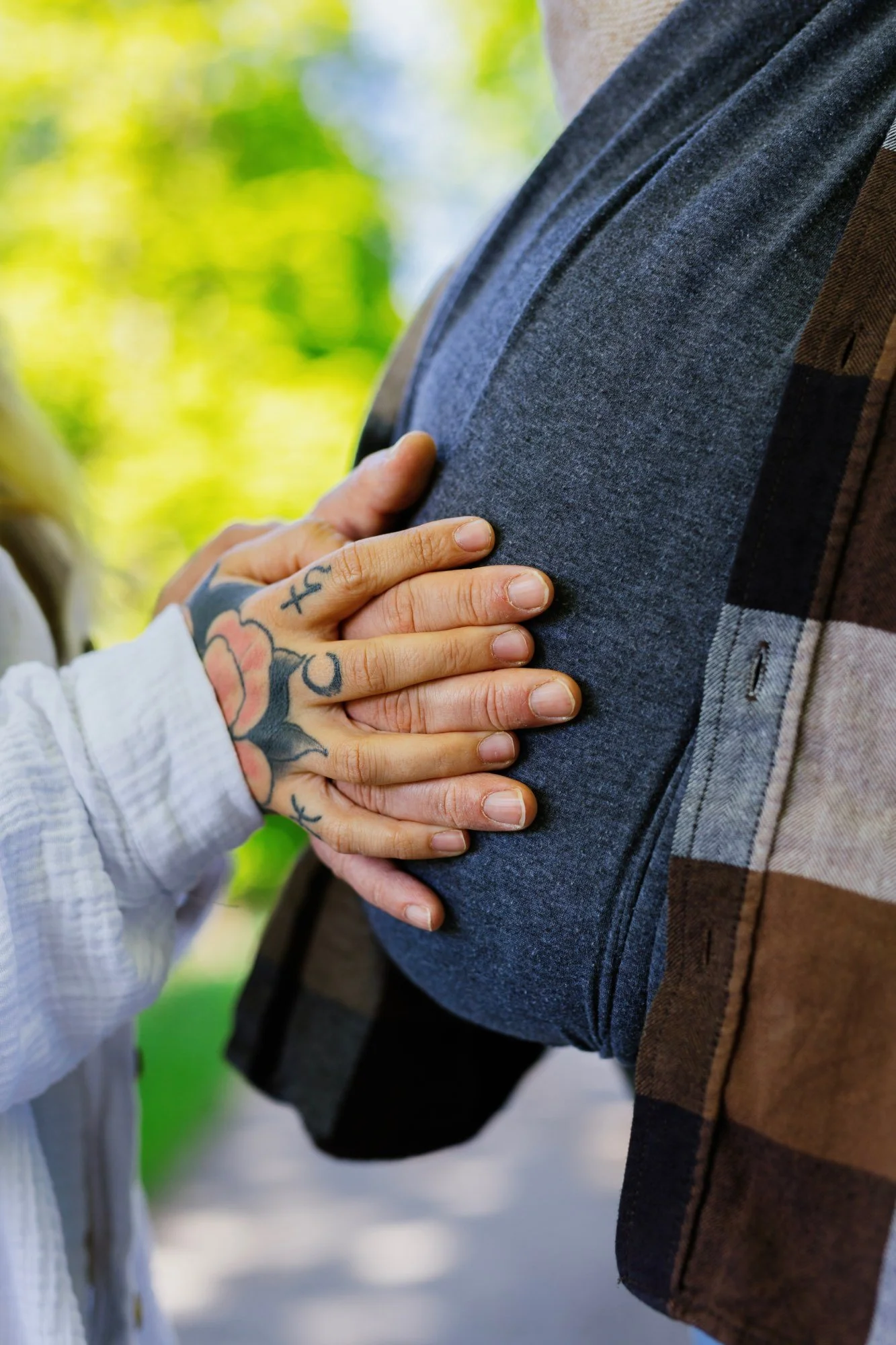 Vater trägt sein Baby in einem Tragetuch, die Hand der Mutter hält es zärtlich.