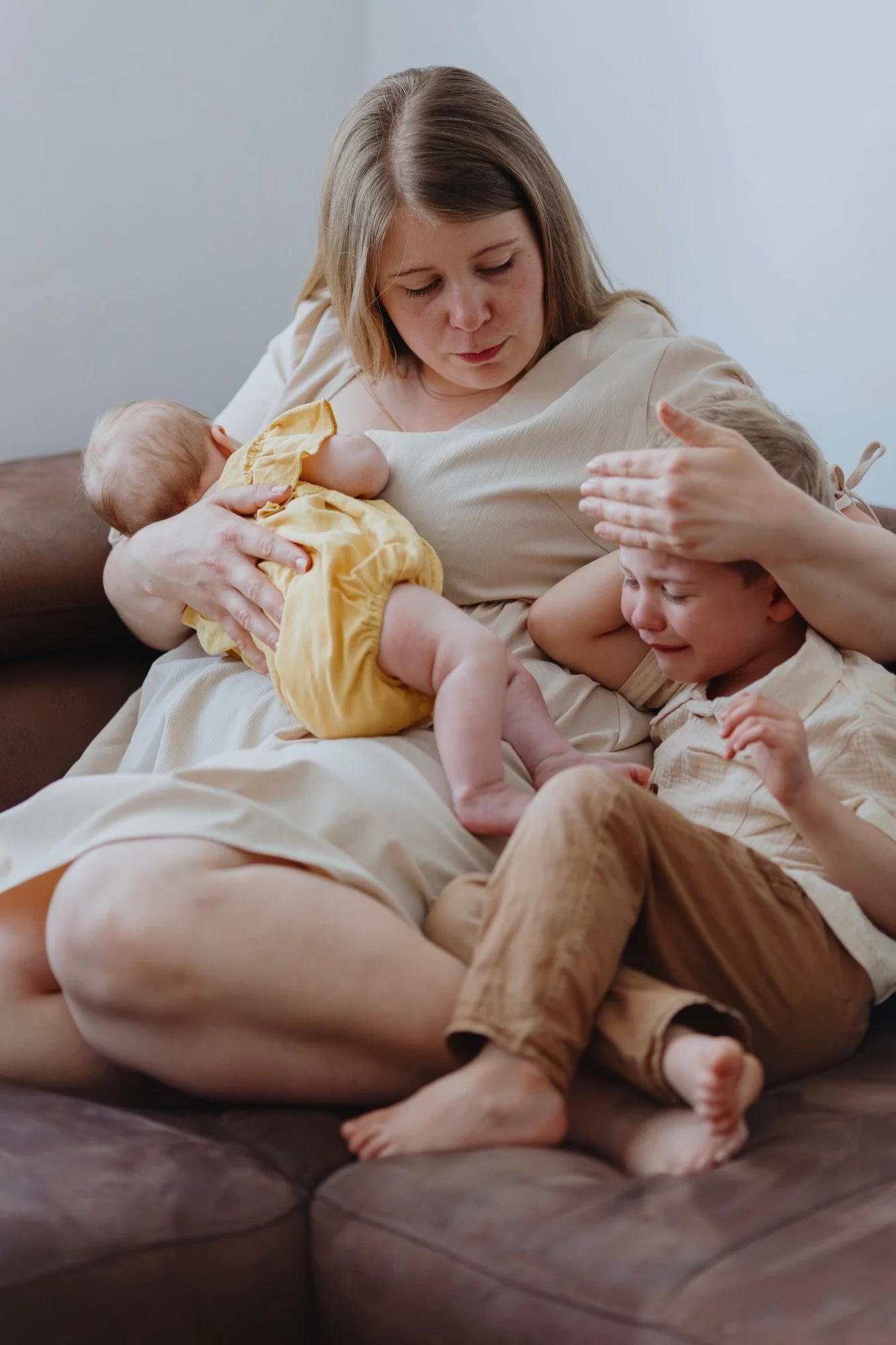 Mutter mit schlafendem Neugeborenen tröstet ihr weinendes Kleinkind auf dem Sofa, Familienfotografie.
