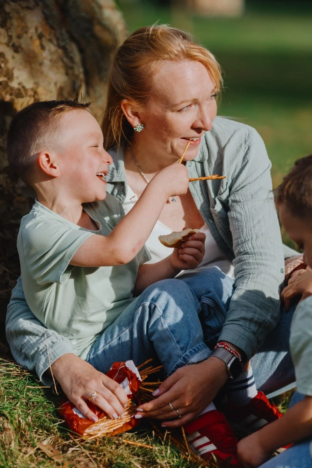 Lachender Junge füttert seine Mutter beim Picknick mit einer Salzstange.